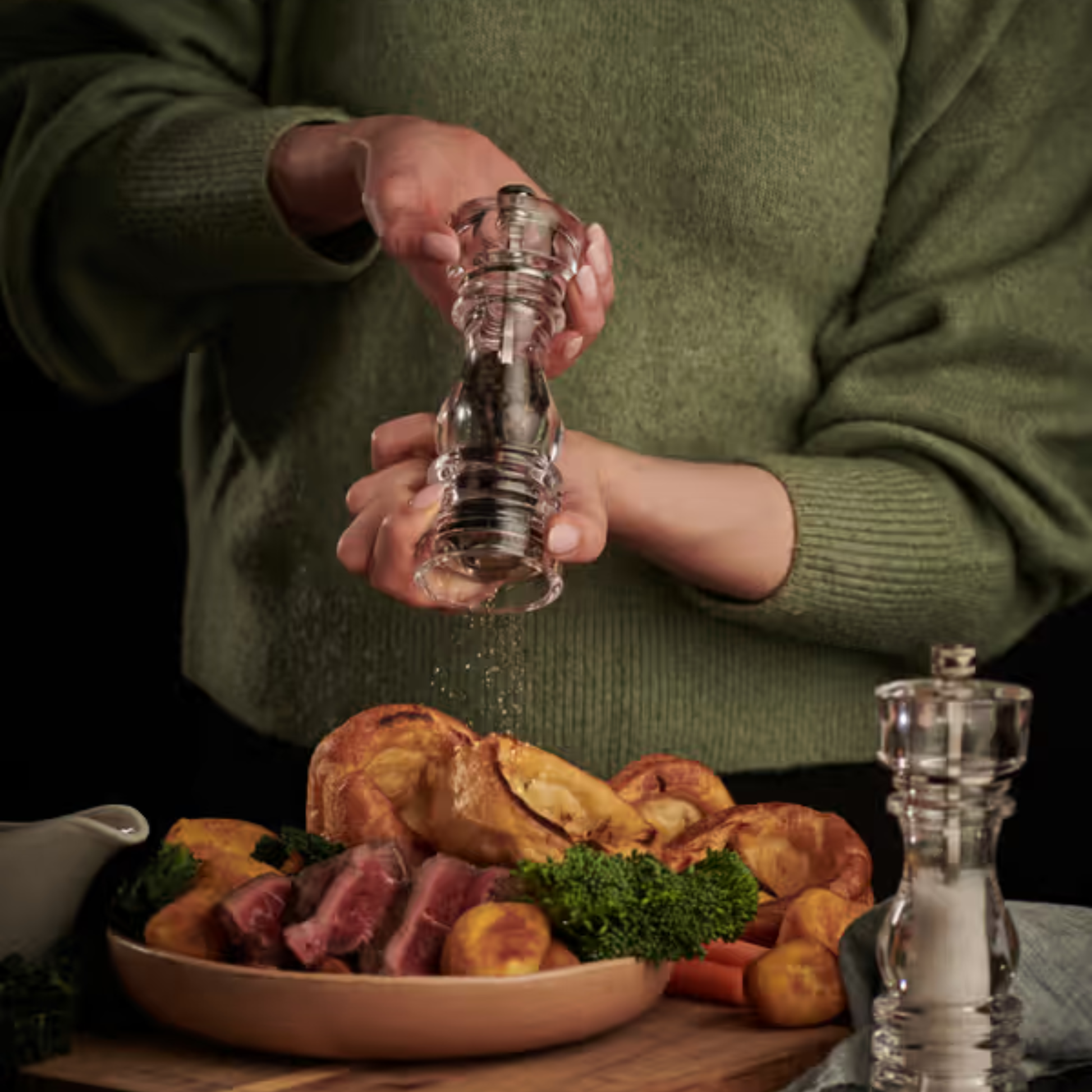 Woman using pepper mill from Cole & Mason London acrylic, 18cm, durable clear body with Precision+ carbon steel and ceramic mechanisms, classic yet modern design with lifetime guarantee.