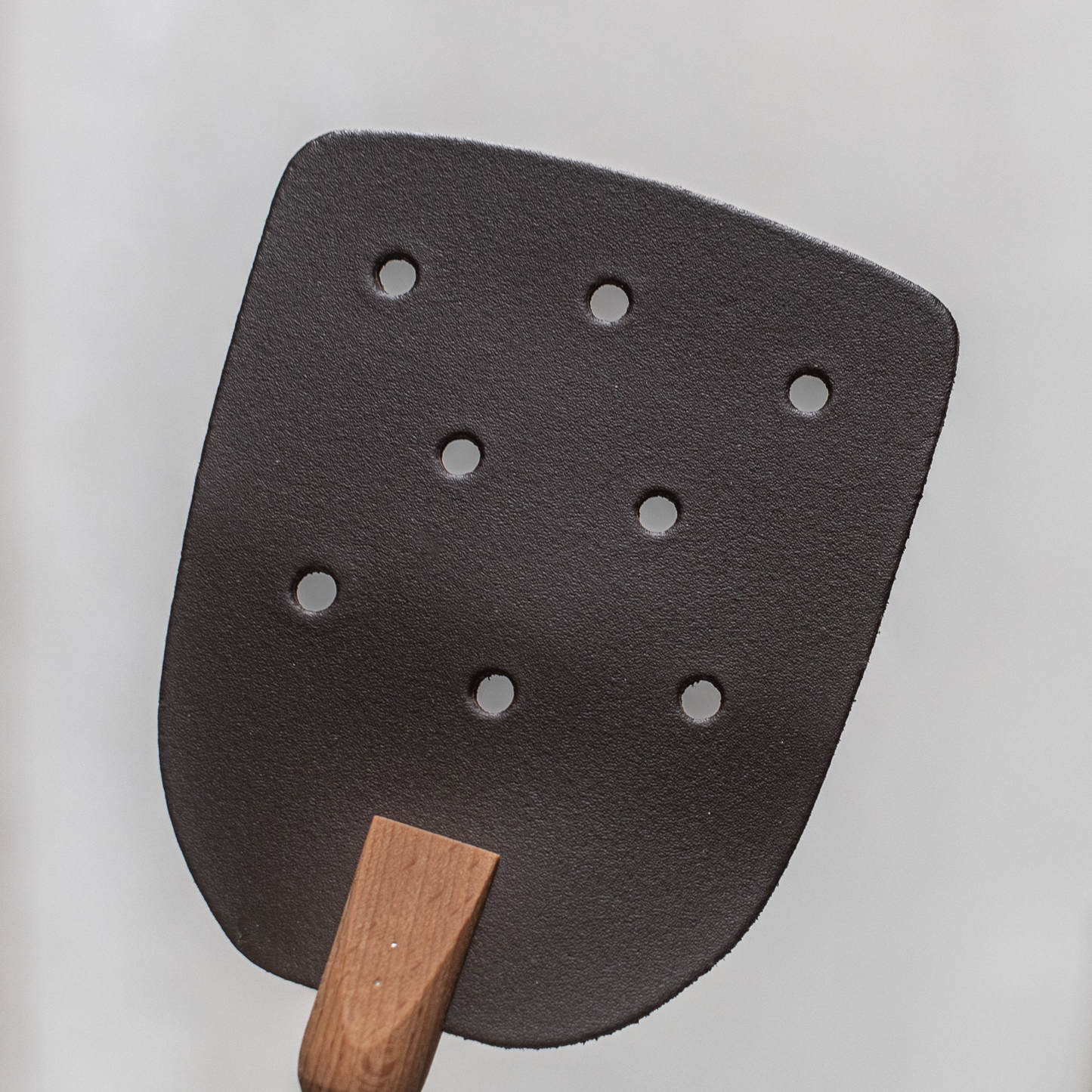 Close up on the holes of the head of Fathom natural leather fly swatter with beechwood handle, 53cm durable and gentle insect control tool for kitchens, patios, and outdoor dining.