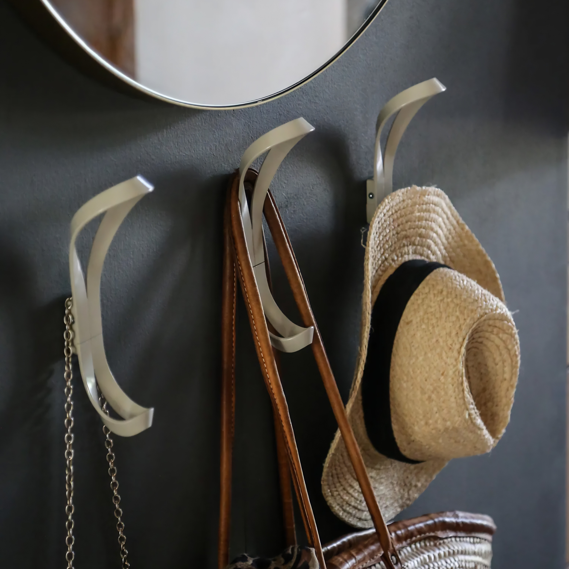 Essem Endless Hook Beige Grey designed by Anna von Schewen from recycled aluminum hung on the wall showing bags hung on it on the back side and hat on the front side.