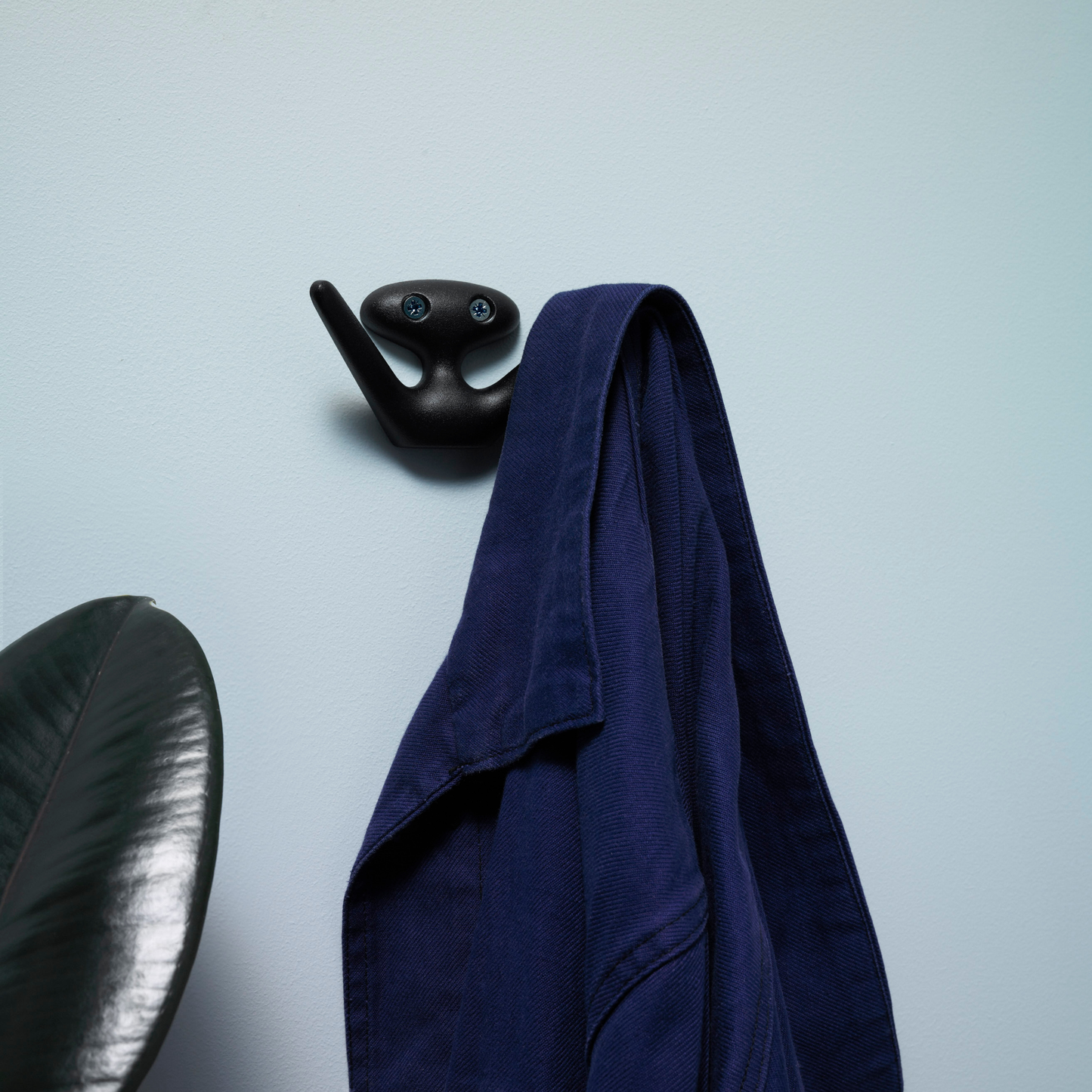 Hung on the wall, the Essem Mama Hook Black designed by Jonas Bergfeldt, made from recycled aluminum featuring a chartacterful hook with open arms.