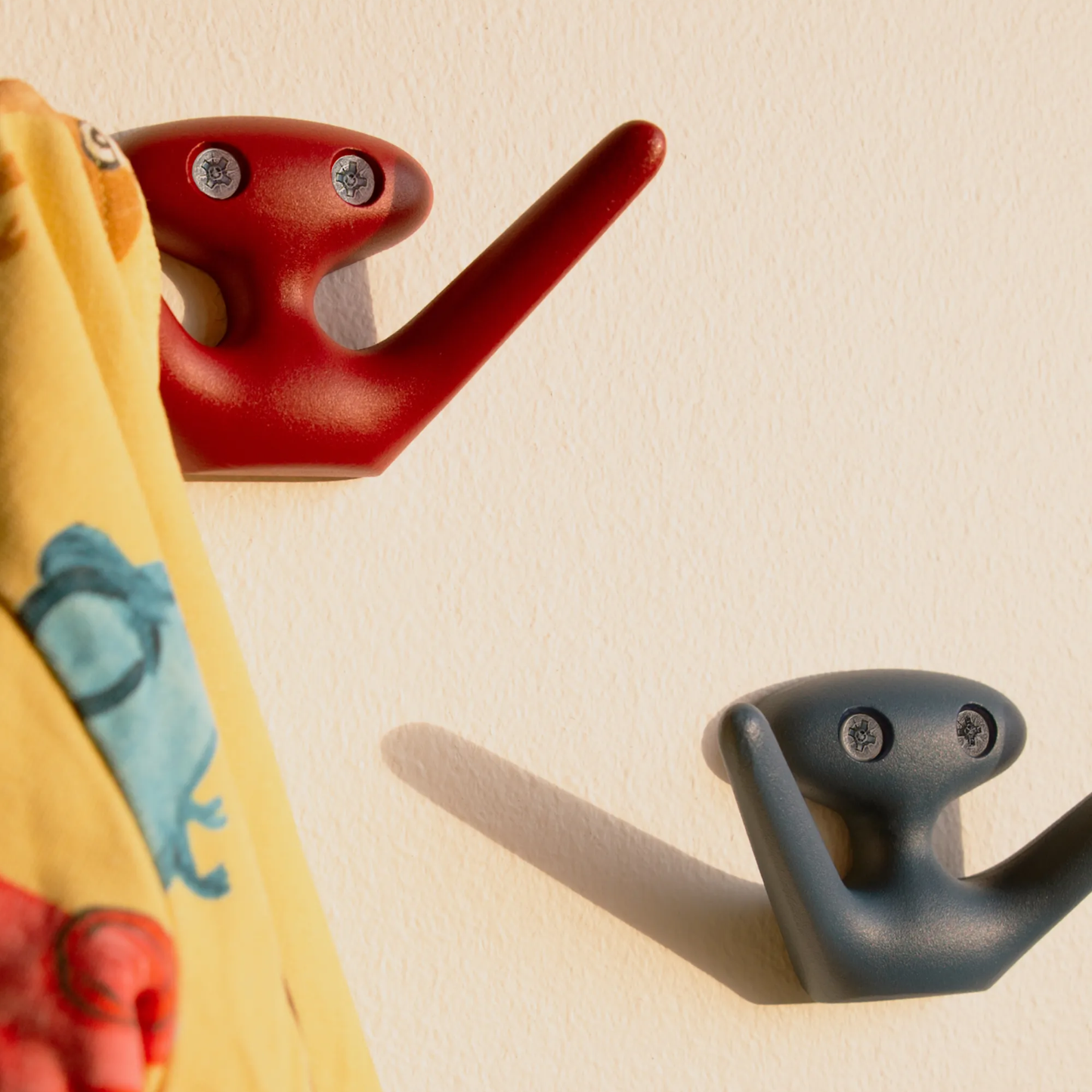 Hung on the wall, the Essem Mama Hook Red designed by Jonas Bergfeldt, made from recycled aluminum featuring a chartacterful hook with open arms.