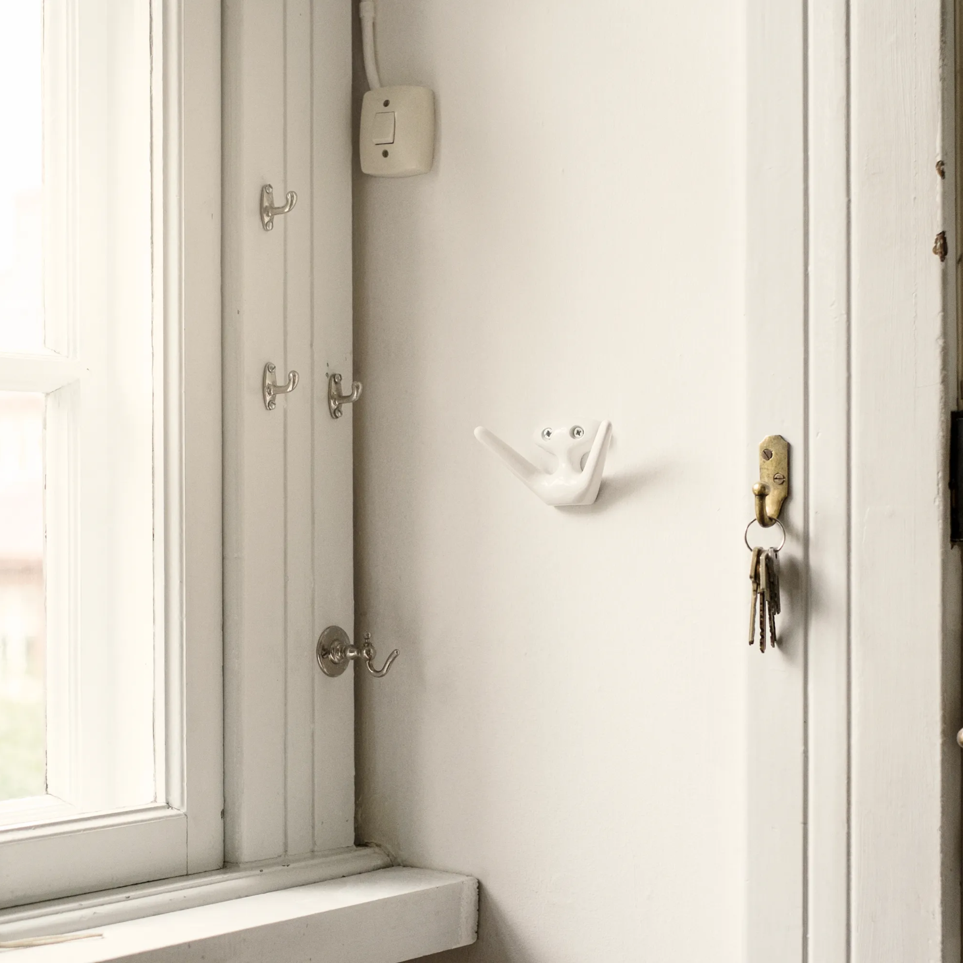 Essem Mama Hook White designed by Jonas Bergfeldt, made from recycled aluminum featuring a chartacterful hook with open arms, hung on the wall.