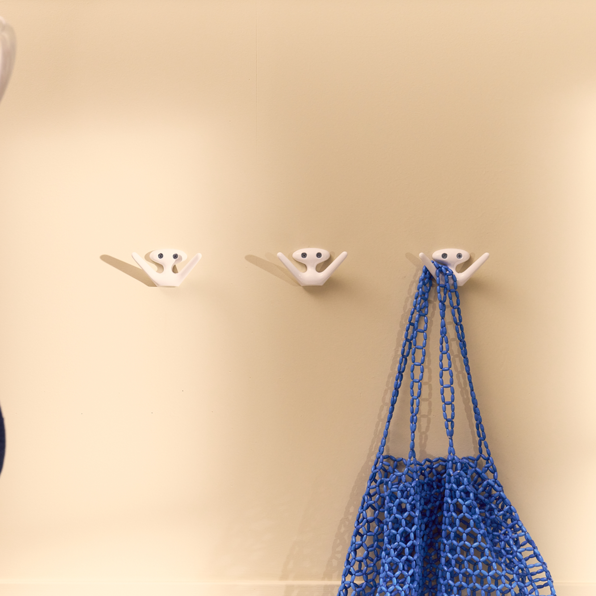 Three Essem Mama Hook White designed by Jonas Bergfeldt, made from recycled aluminum featuring a chartacterful hook with open arms, hung on the wall.