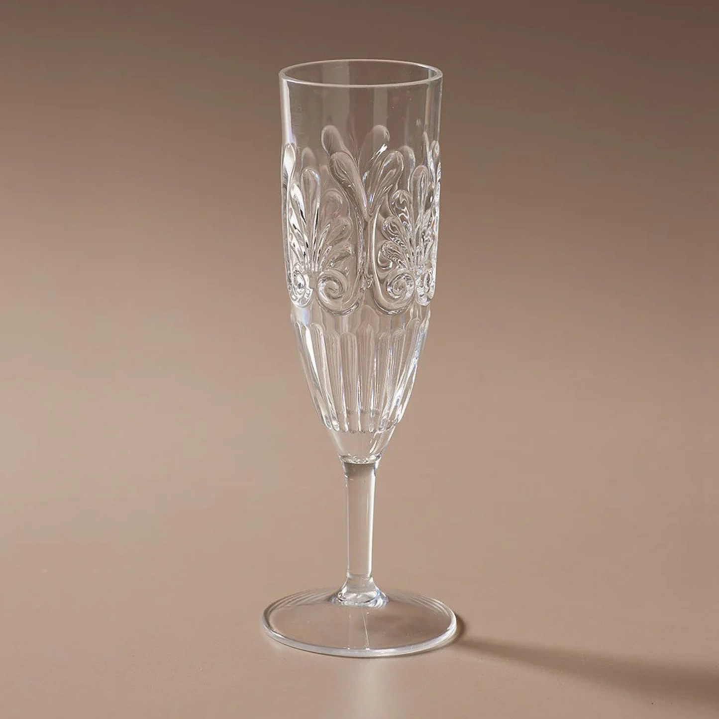 In a brown background Fathom Clear acrylic champagne flute with elegant embossed detailing, glass-like clarity, and shatter-resistant BPA-free material.