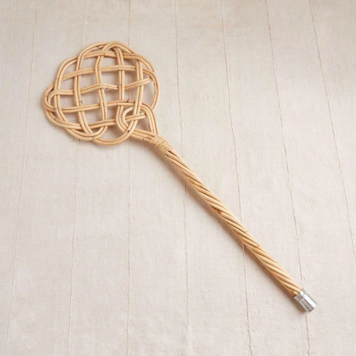 Shown on the floor, Fathom Carpet Beater - Handwoven rattan reed, 75x23cm, durable and splinter-resistant, traditional dust remover for carpets, rugs, cushions, and pillows, handcrafted German cleaning tool, eco-friendly and long-lasting.