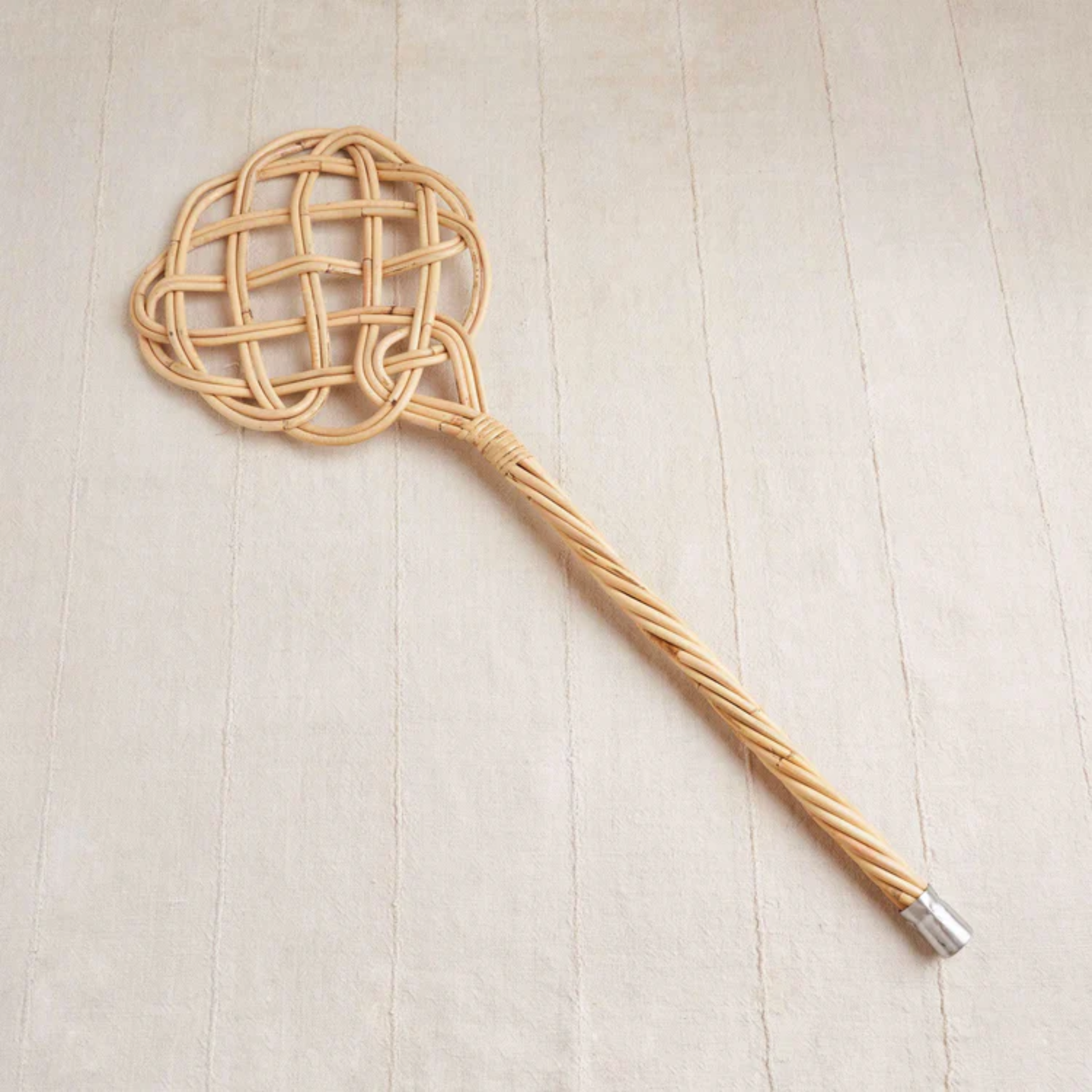 Shown on the floor, Fathom Carpet Beater - Handwoven rattan reed, 75x23cm, durable and splinter-resistant, traditional dust remover for carpets, rugs, cushions, and pillows, handcrafted German cleaning tool, eco-friendly and long-lasting.
