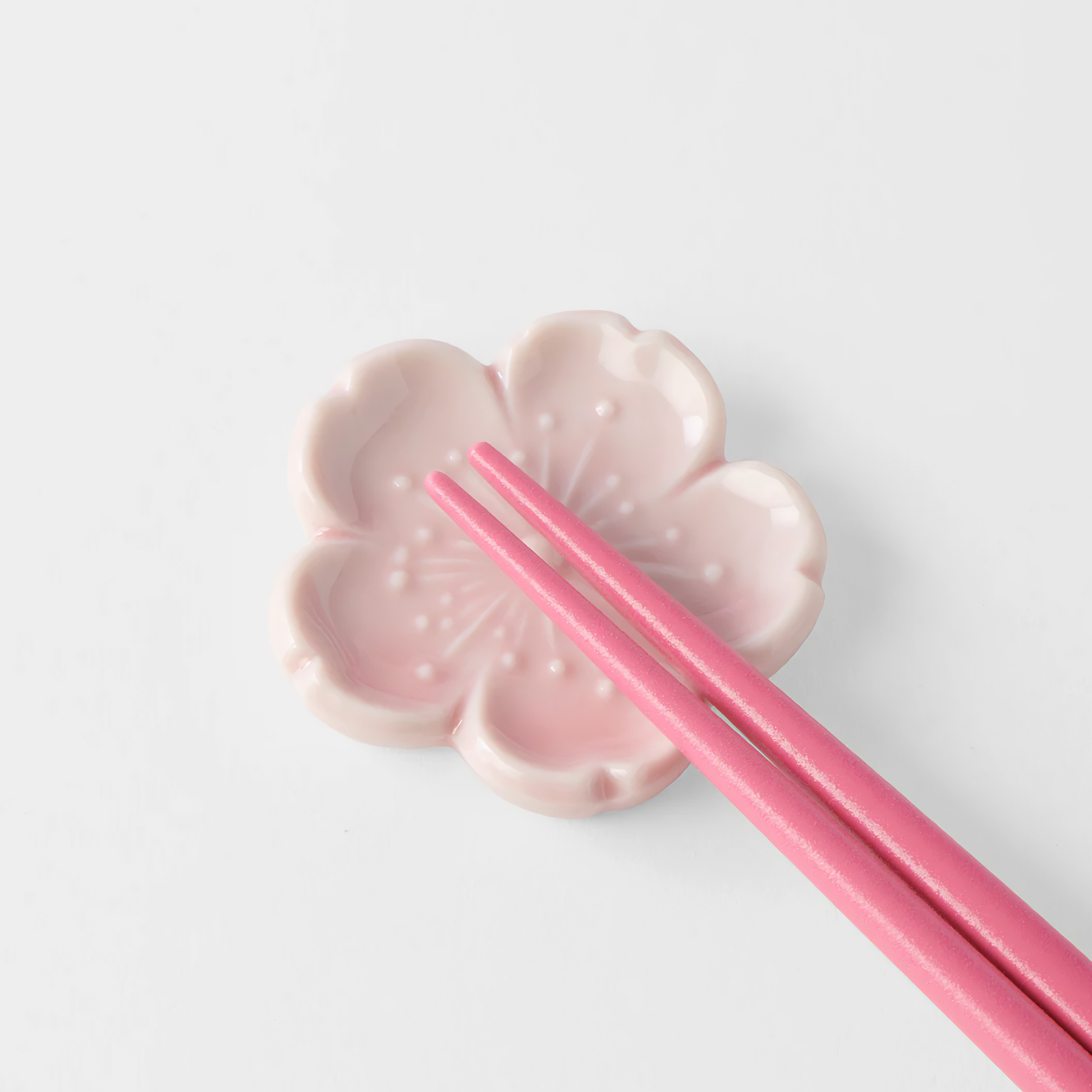 A pair of pink chopstick rested on the Fathom Chopstick Rest Pink Sakura that has soft pink glaze inspired by cherry blossoms and pebble like shape.