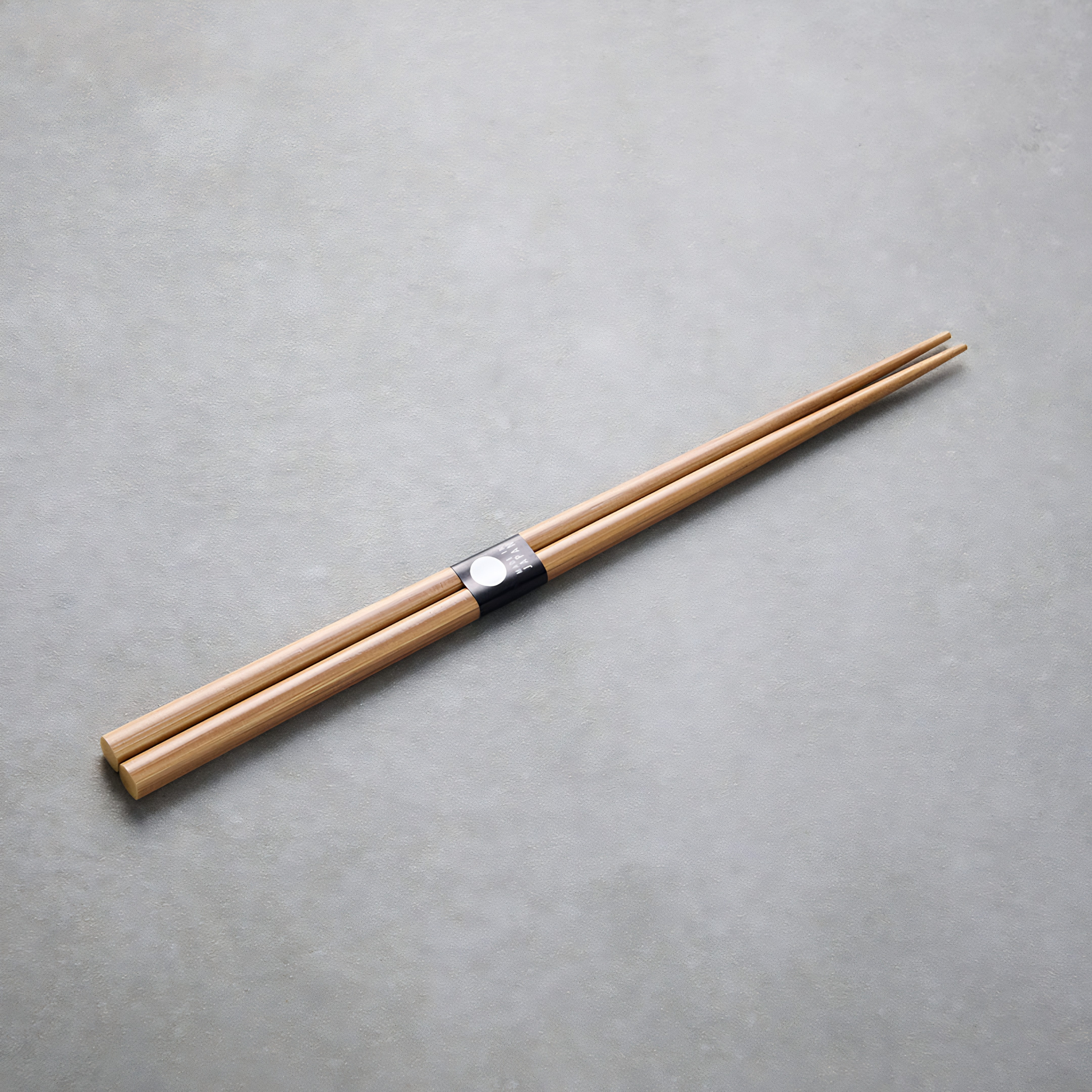 Laid on a gray surface the Fathom Chopsticks Pair Bamboo Brown featuring a clean, understated finish with subtle grain variation.