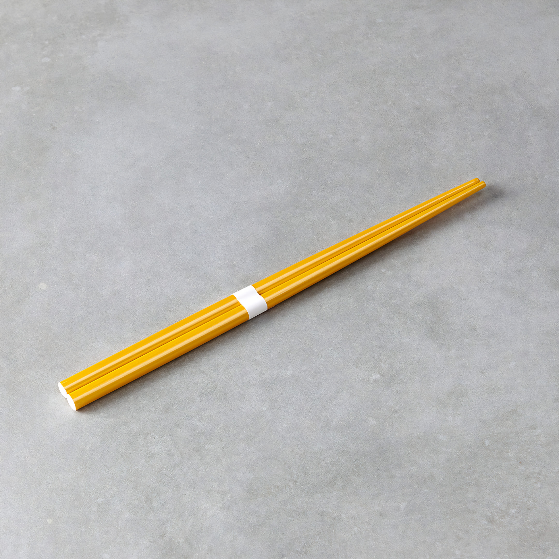 Laid on a gray surface the Fathom Chopsticks Pair Lacquered Gold, sleek finish with a white accent.