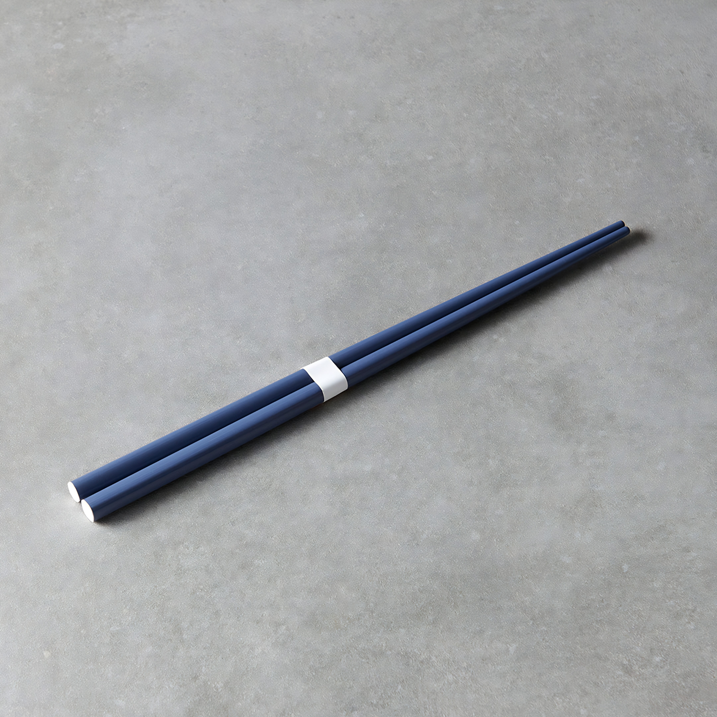 Laid on a gray surface the Fathom Chopsticks Pair Lacquered Navy blue rich finish with subtle white accent.