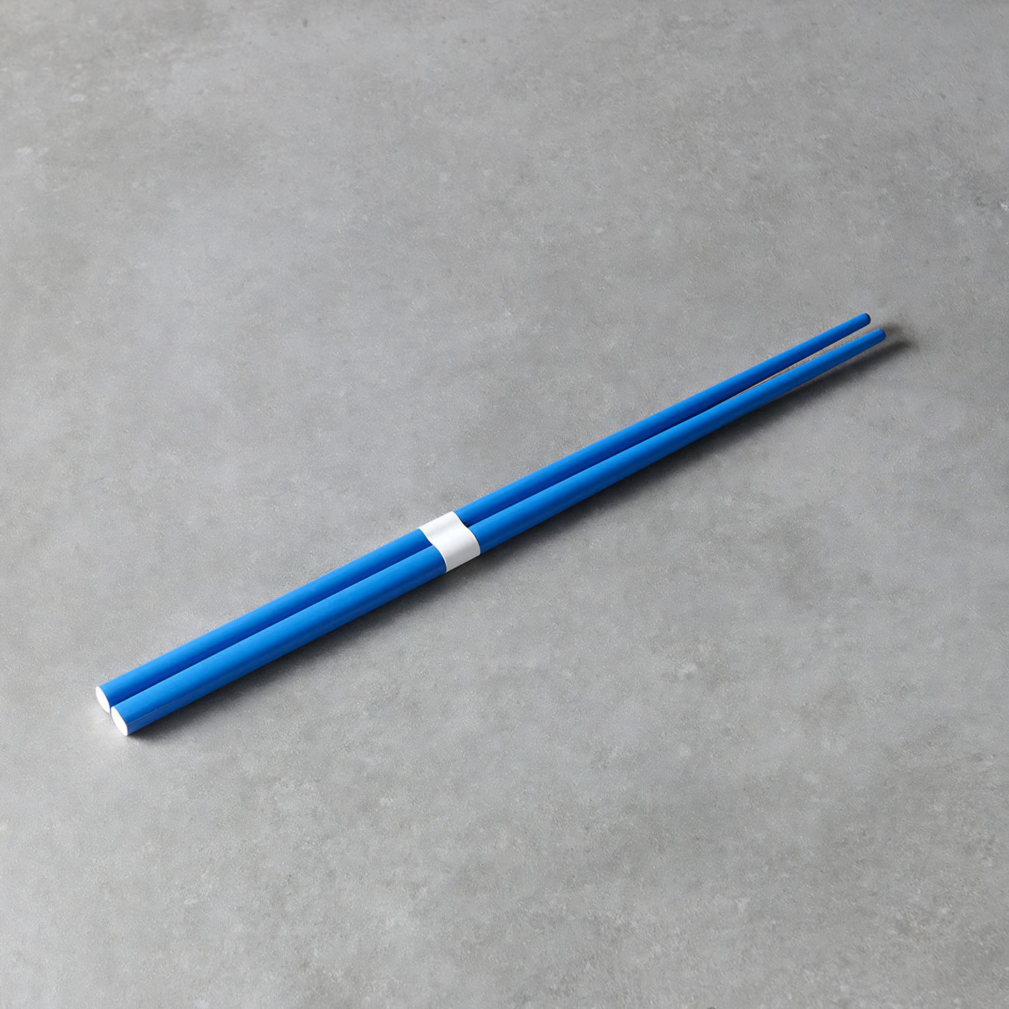 Laid on a gray surface the Fathom Chopsticks Pair Lacquered Royal blue finish with subtle white accent for smooth and glossy surface.
