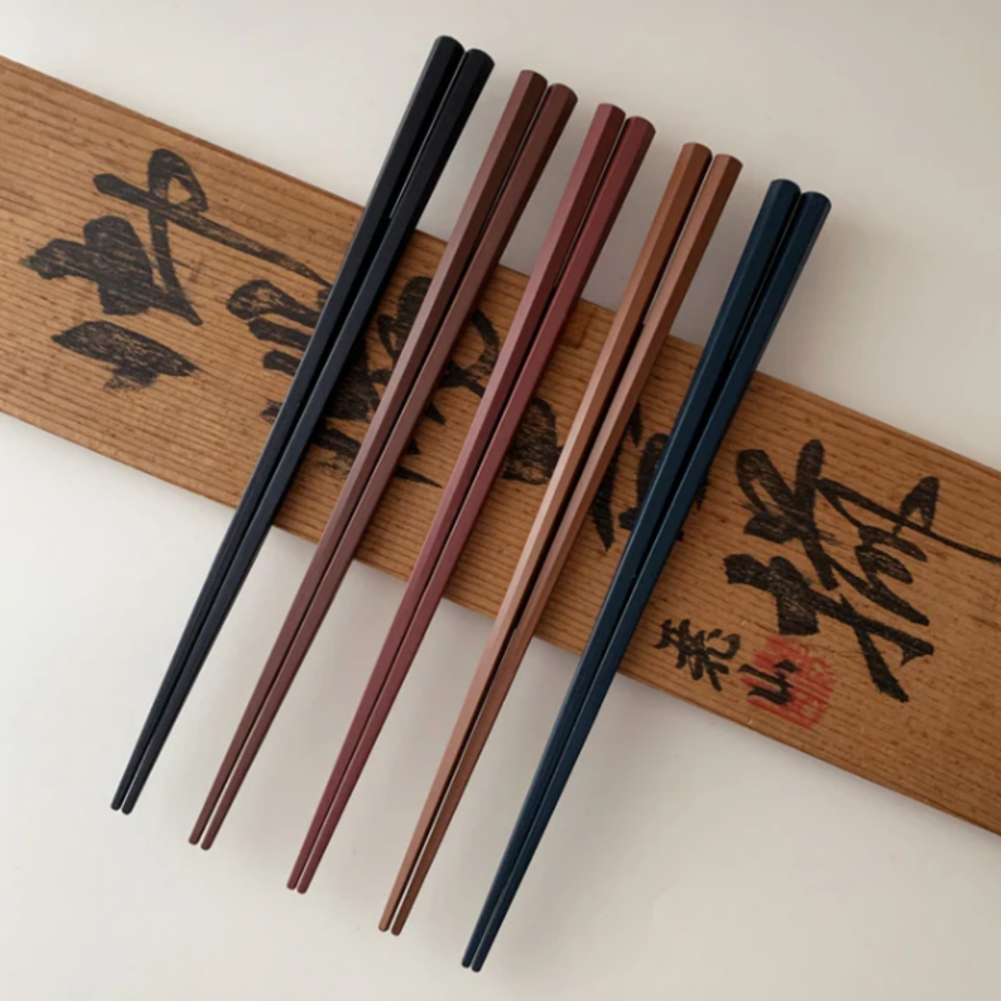 Shown on a wood Fathom Kyoto Chopsticks Set of 5 - Timber-tone resin chopsticks, 23cm long, hexagonal shape with matte finish for non-slip grip, dishwasher safe.