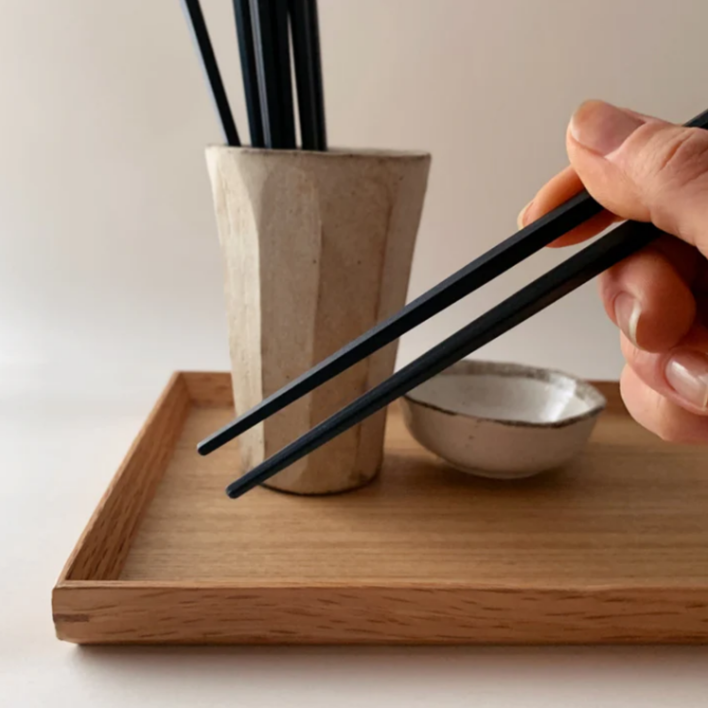 A pair of Kyoto chopsticks being held from Fathom Kyoto Chopsticks Set of 5 - Timber-tone resin chopsticks, 23cm long, hexagonal shape with matte finish for non-slip grip, dishwasher safe.