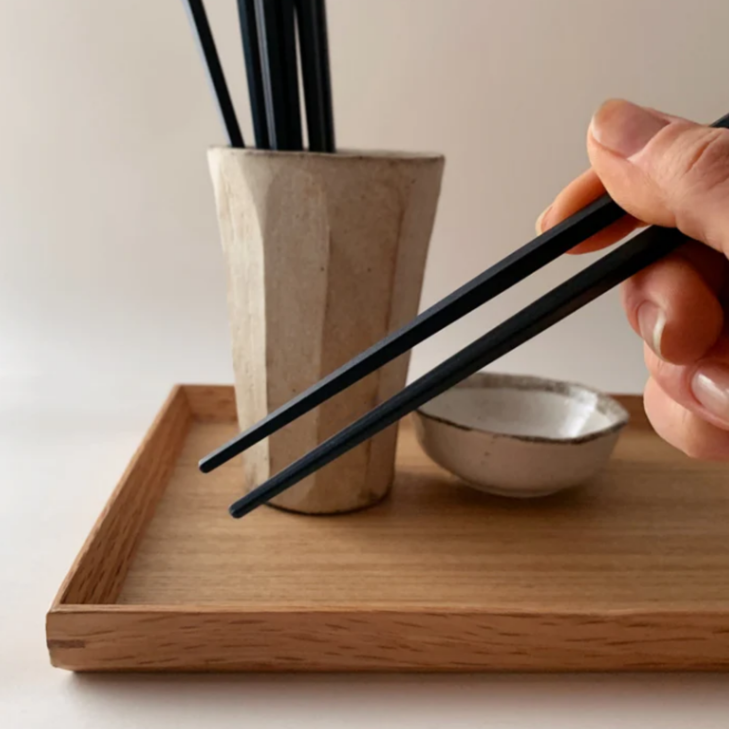 Shown being held on a finger showing its tips from a pair of chopsticks from Fathom Osaka Chopsticks Set of 5 - Black resin chopsticks, 23cm long, hexagonal shape with matte non-slip finish, comfortable grip, dishwasher safe.