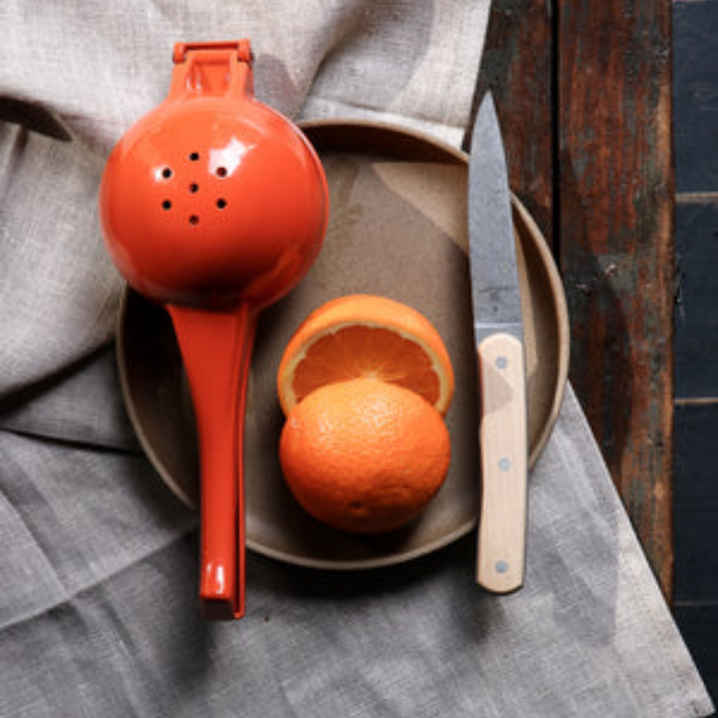 Orange metal Citrus squeezer back view on plate with grapefruit on wooden table with linen cloth