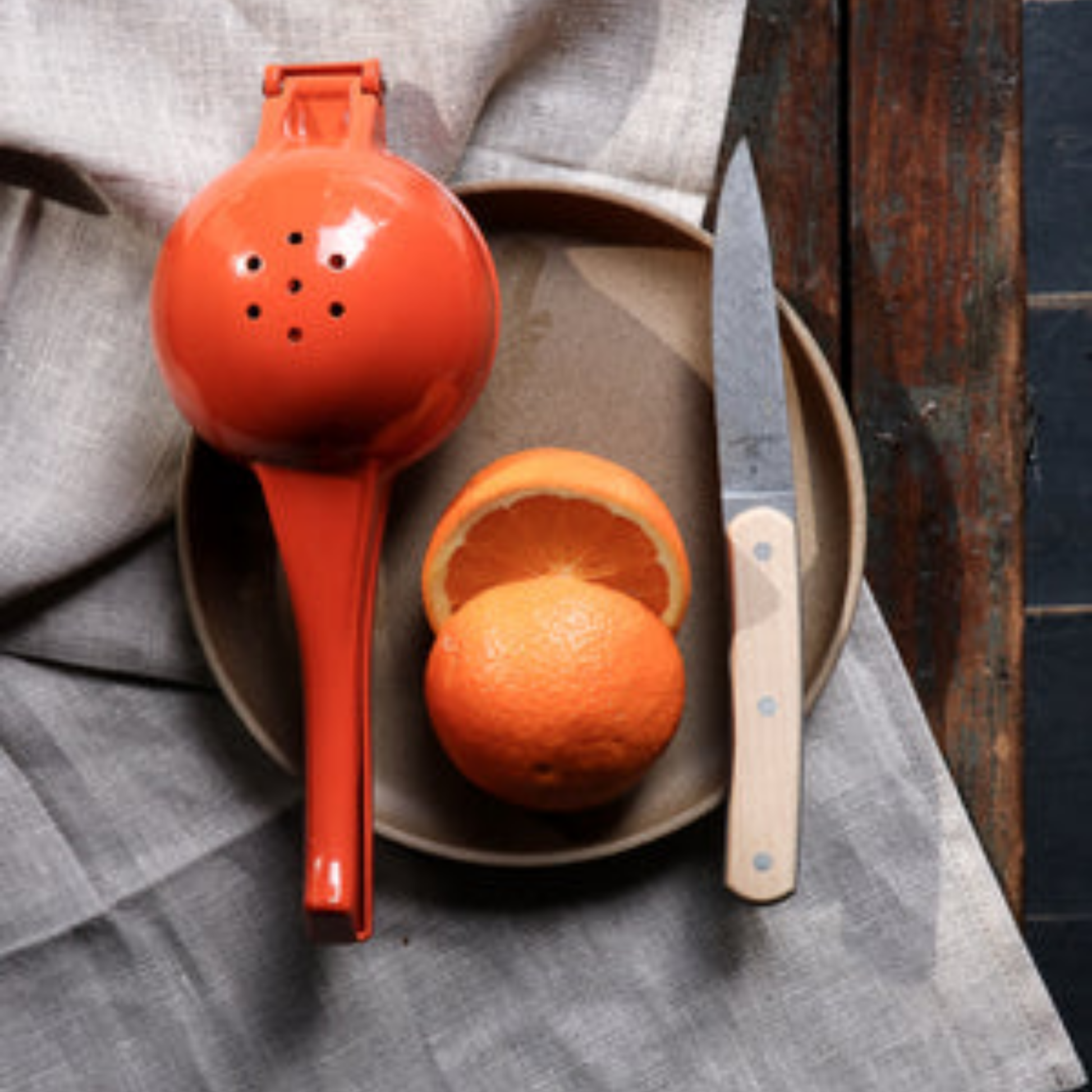 Orange metal Citrus squeezer back view on plate with grapefruit on wooden table with linen cloth