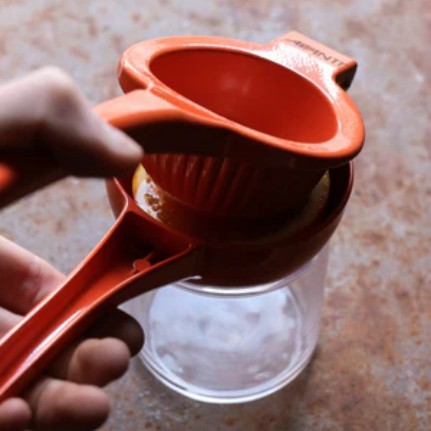 Close up of orange metal Citrus squeezer angled top view squeezing juice in to glass