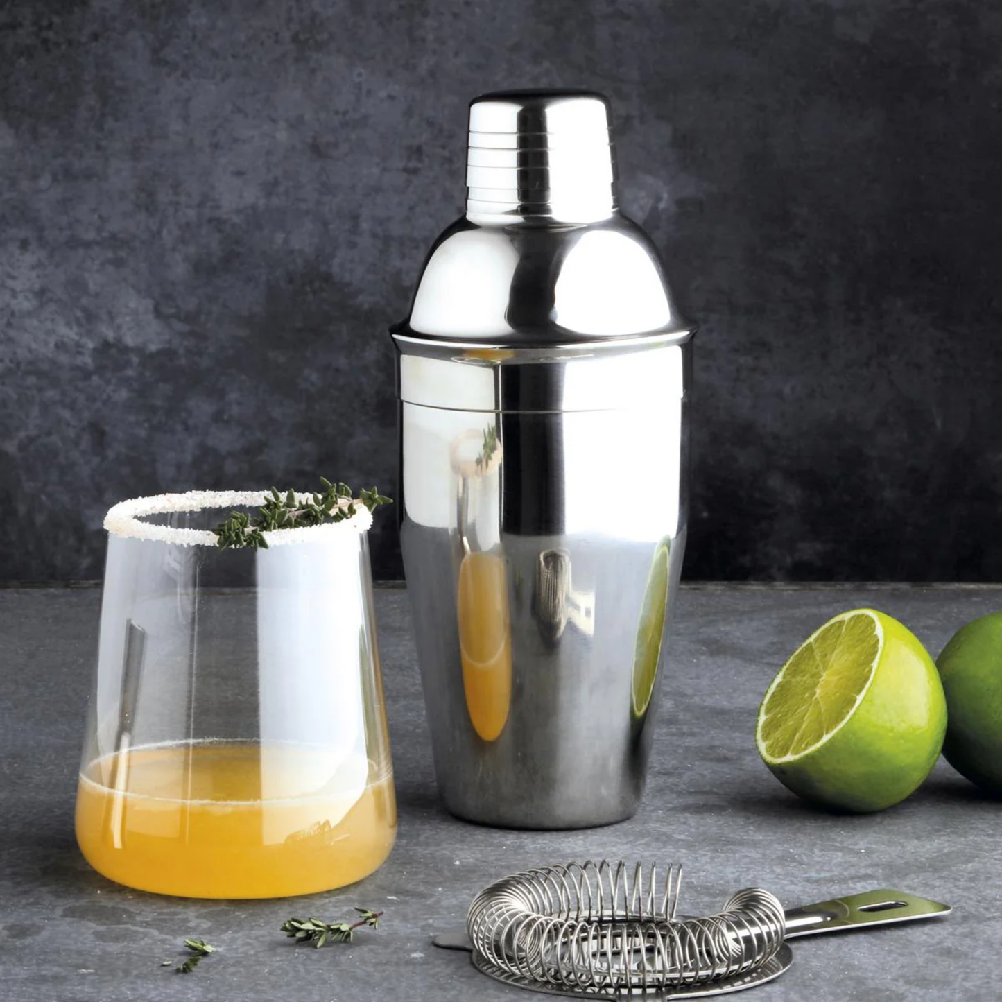 Metal cocktail shaker 500ml front view on diaply with citrus fruits and cocktail in glass