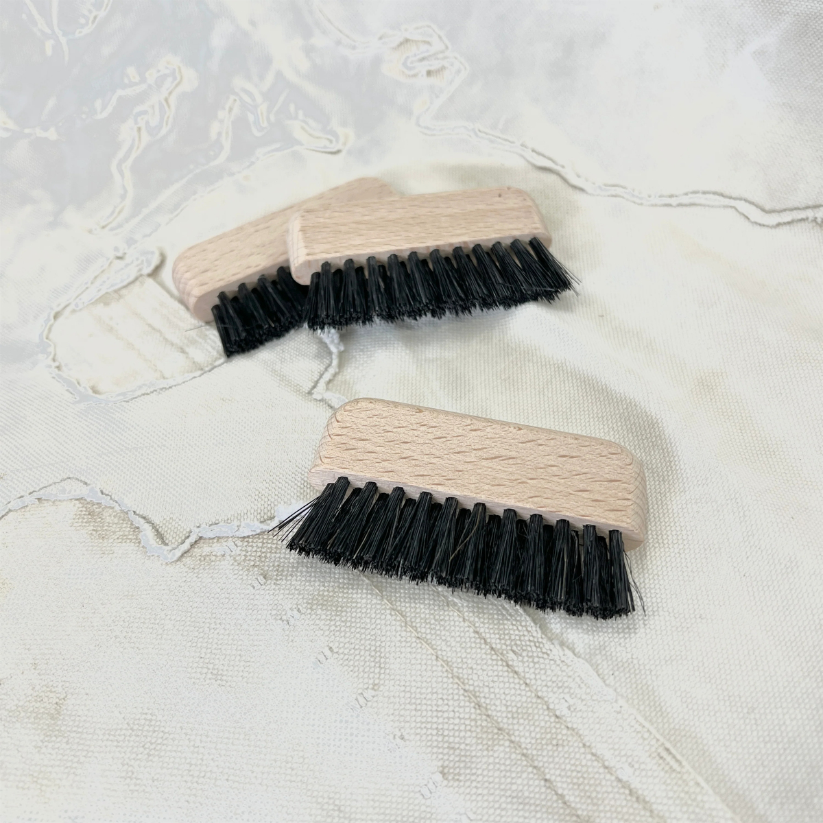 Two Fathom Computer Brushes with black bristles rest on a light fabric background with stitched patterns.