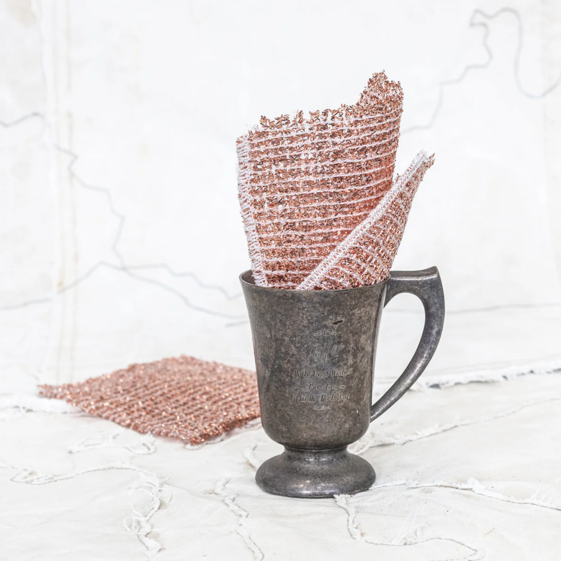 Cloth copper cop scrubber in a mug from Fathom Copper Pot Scrubbers & Sponges - German-made cleaning tools with fine copper threads, remove tough dirt without scratching, ideal for pots, pans, stoves, glass, and sinks, available in cloth, sponge, and scourer types.