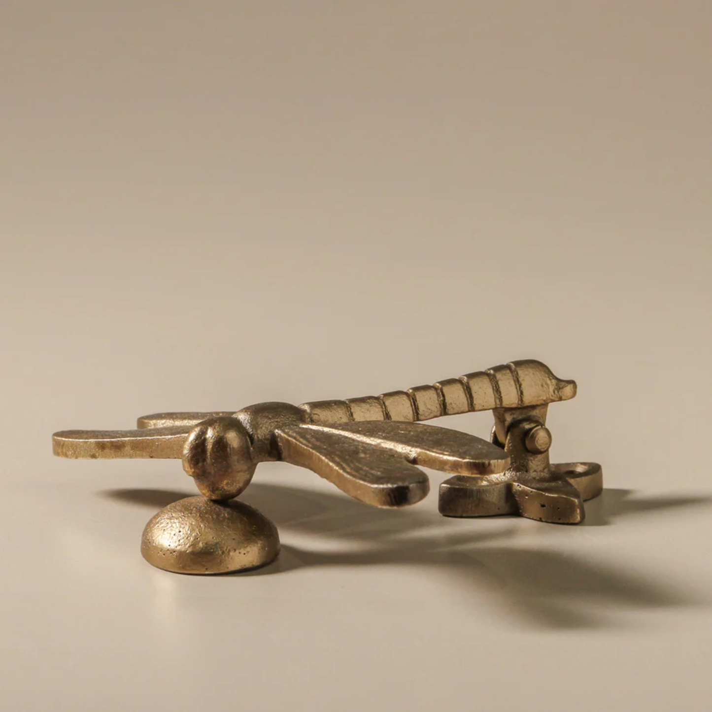 Side view of Fathom dragonfly-shaped door knocker, antique brass iron with detailed wings and sculptural texture, handcrafted and includes strike plate for mounting.