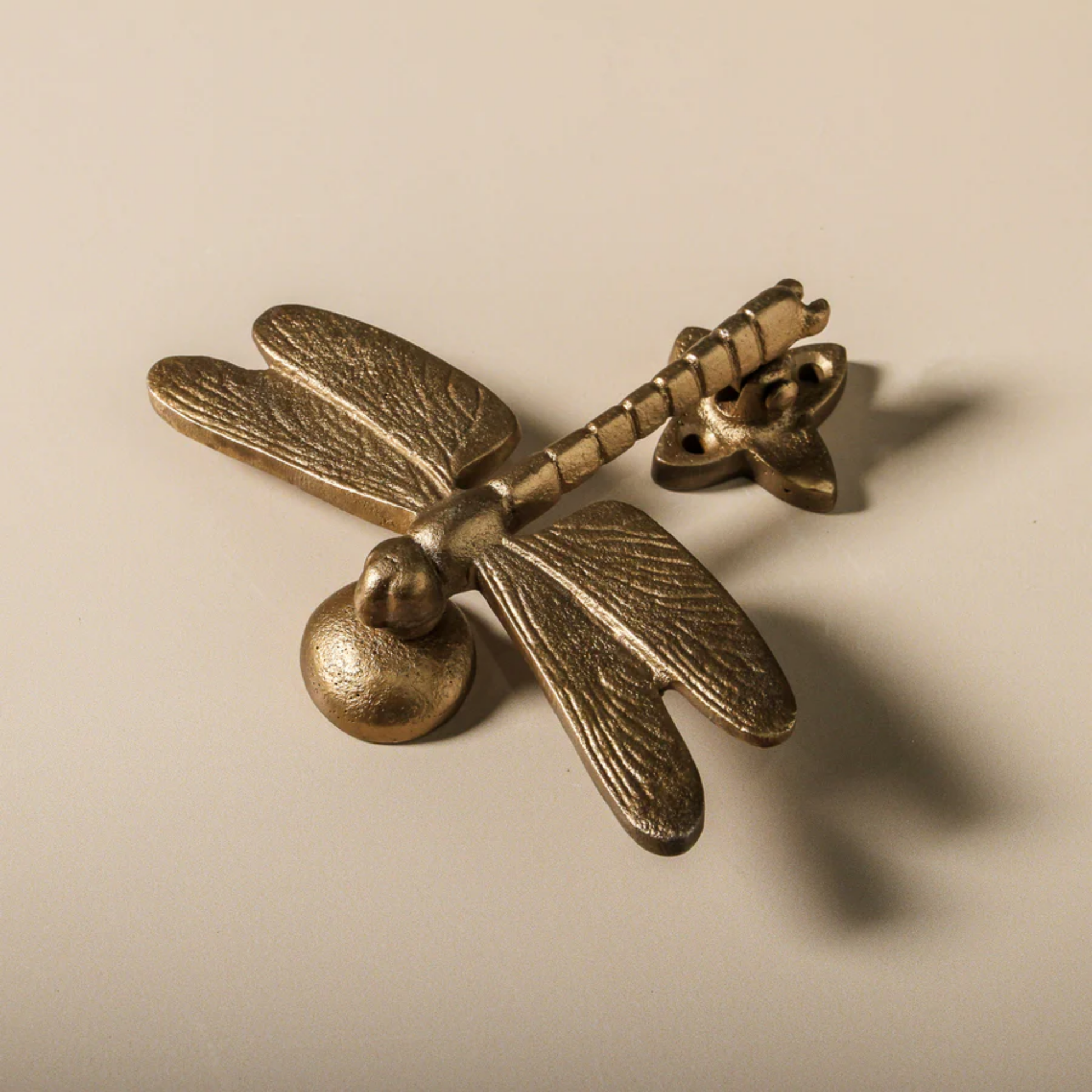 Top view of Fathom dragonfly-shaped door knocker, antique brass iron with detailed wings and sculptural texture, handcrafted and includes strike plate for mounting.
