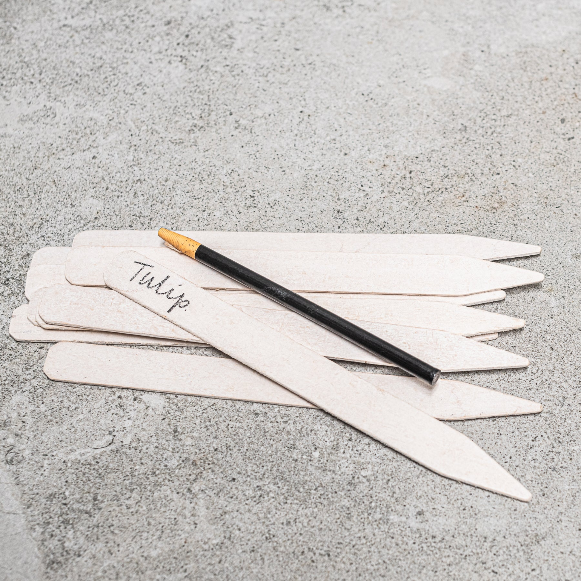 White garden lables with black pencil sprawled out on concrete bench