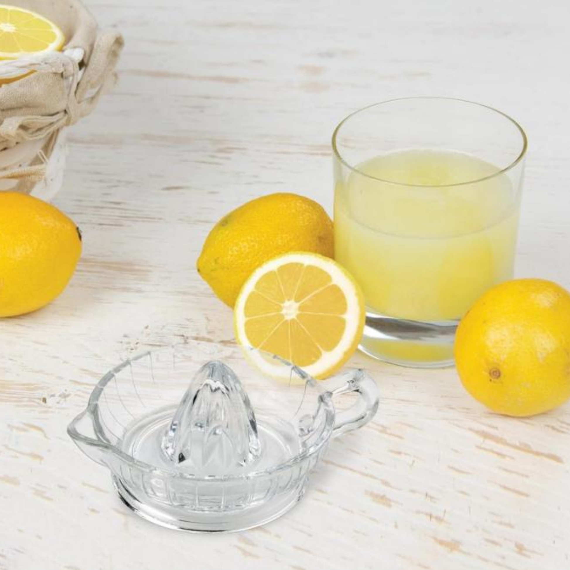 Glass citrus juicer and display with lemons and glass of lemon juice on whit wooden table 