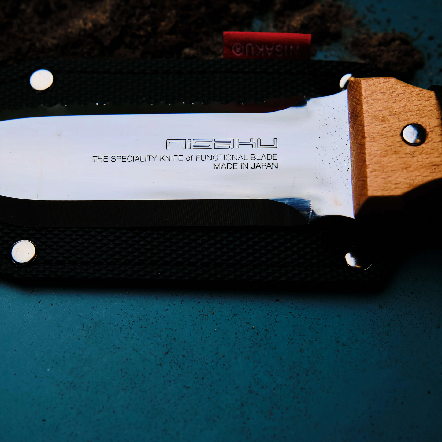 Close up view on the logo on the blade from Fathom Hori Hori Compact Japanese Garden Knife with Sheath with blade as stainless steel and 70mm, with varnished hardwood and synthetic leather sheath.
