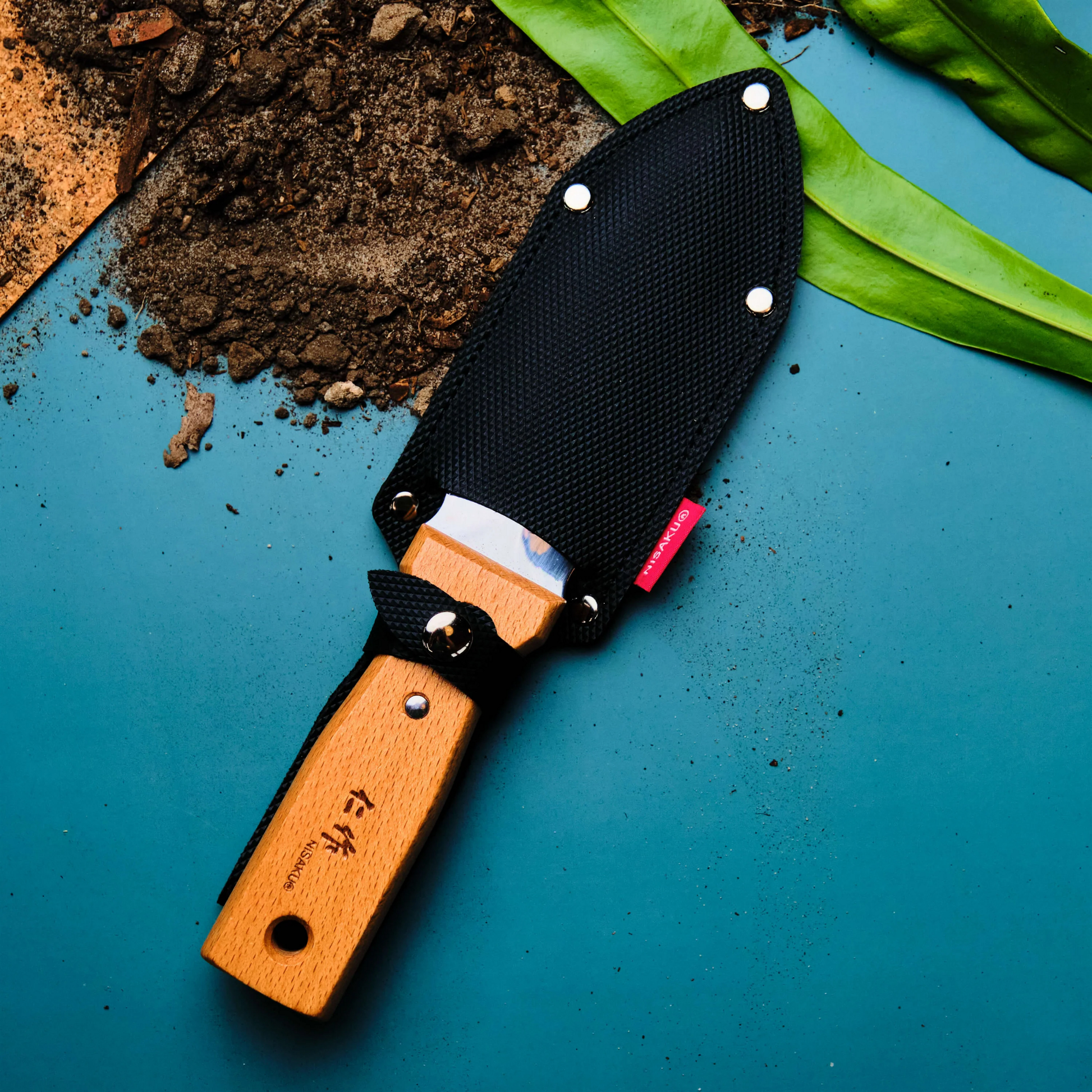 Top view of the sheathed knife which is the Fathom Hori Hori Compact Japanese Garden Knife with Sheath with blade as stainless steel and 70mm, with varnished hardwood and synthetic leather sheath.