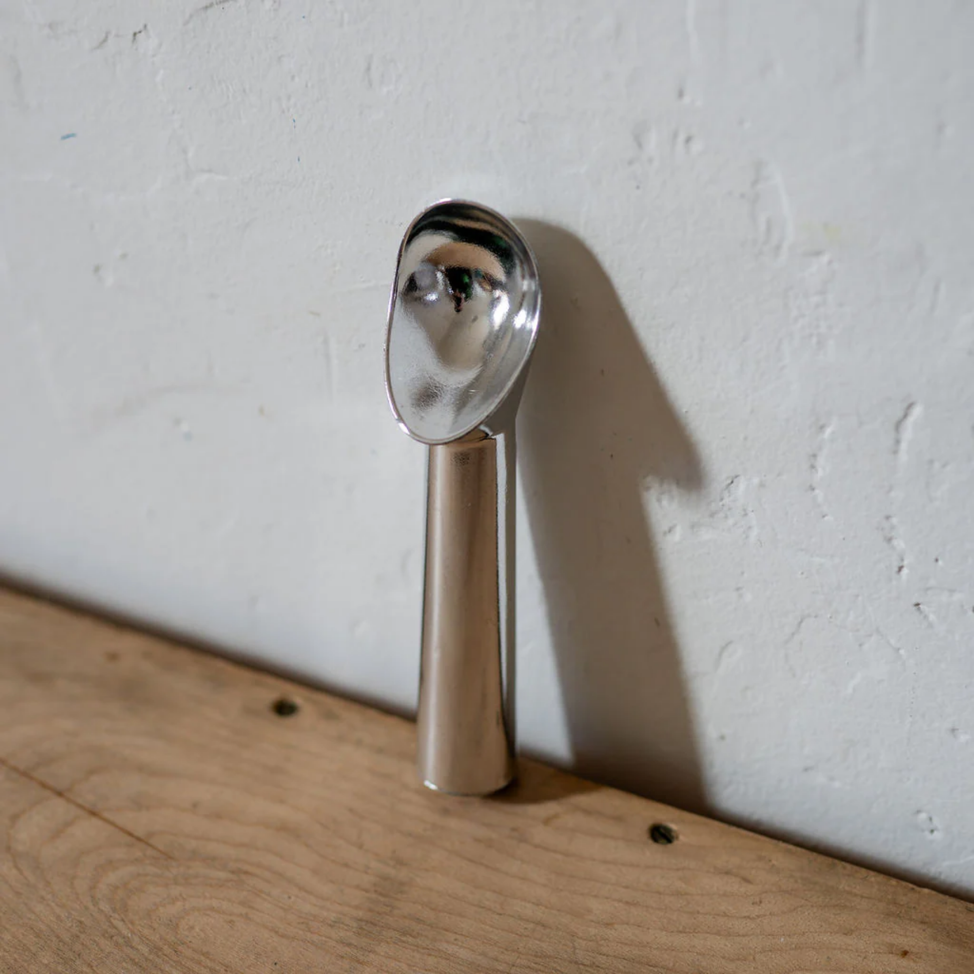 Aliminium ice cream scoop angled front view on wooden countertop