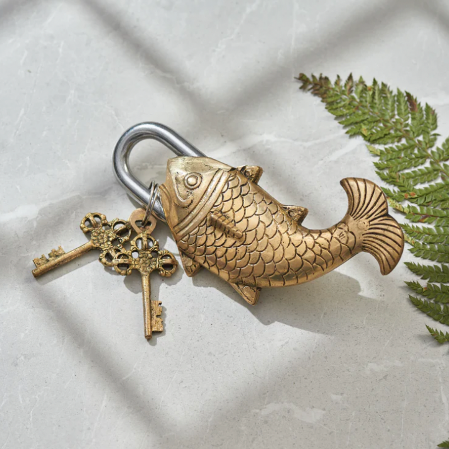 Indian brass fish padlock with keys lying flat on marble counter top