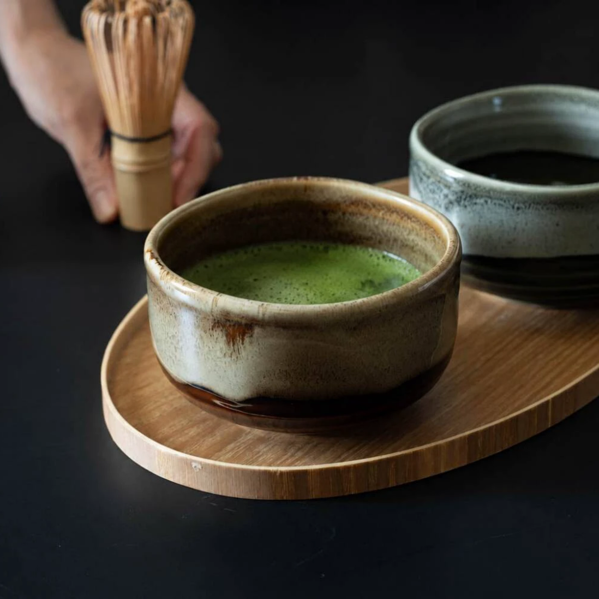 Fathom Japanese Mino Ware Matcha Bowl Miyajima Amber Ceramic, hand-crafted with a rich, lustrous glaze, shown on a wooden surface with a matcha, a whisk and another bowl.
