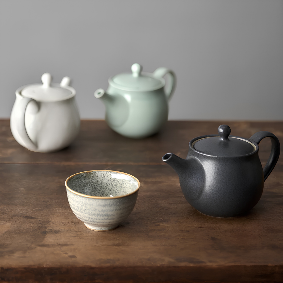 On the table with sake cup and other pots with the Fathom Japanese Teapot in matt black, ceramic with satin glaze, rounded form and graceful spout for smooth pouring.