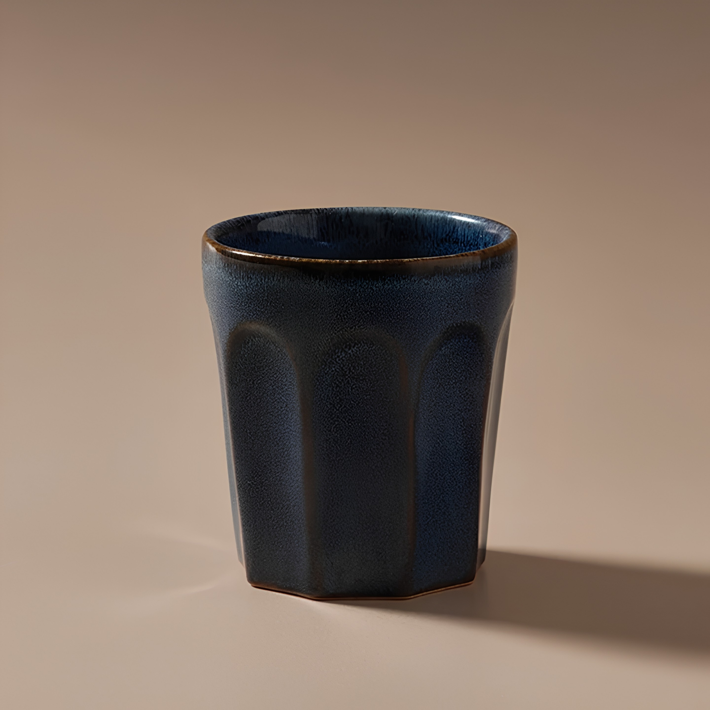 Front view with a background of Fathom Latte Cup Navy stoneware that is handcrafted with reactive glazes of earthly hues finish.