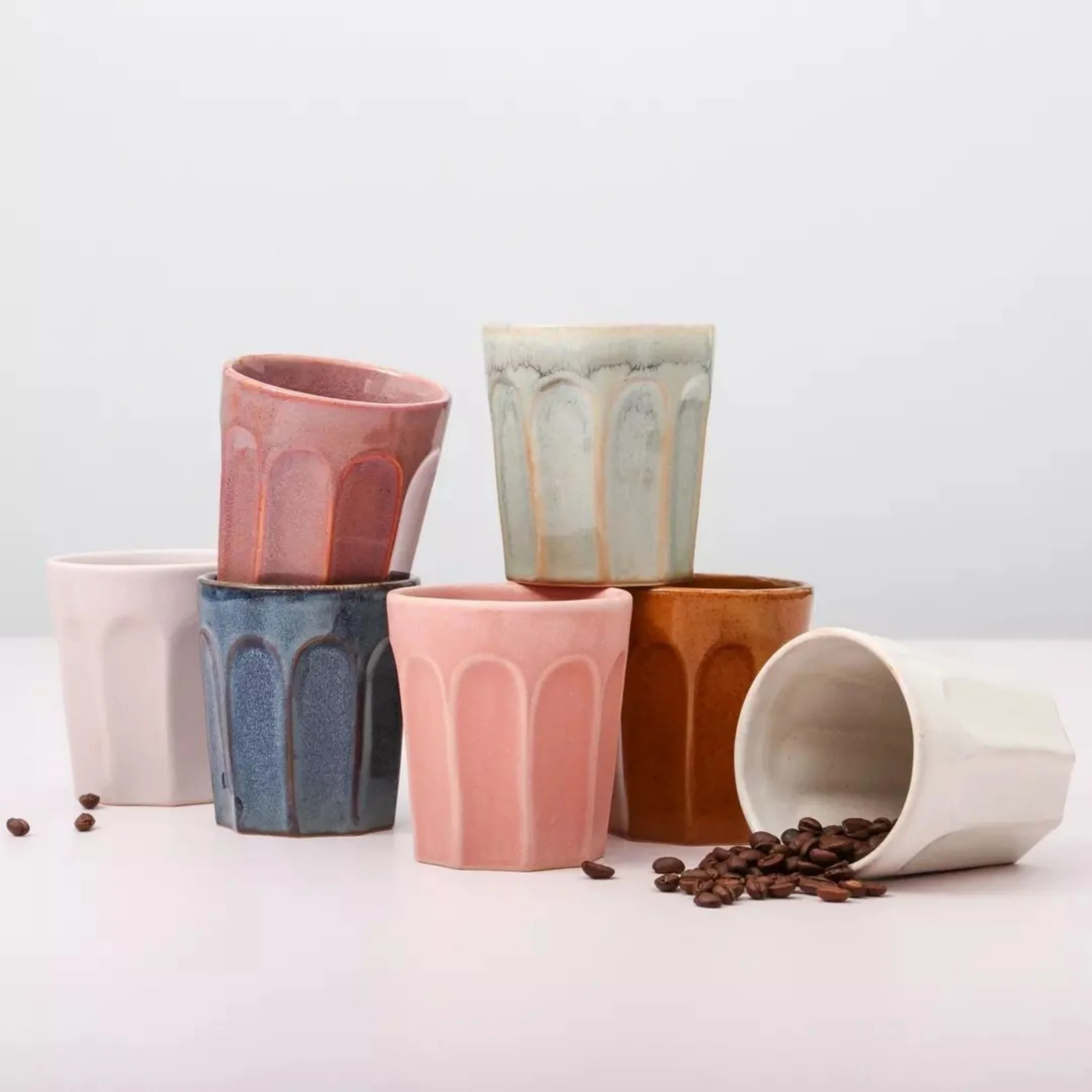 Collection of latte mugs all stacked together on white surface with coffee beans