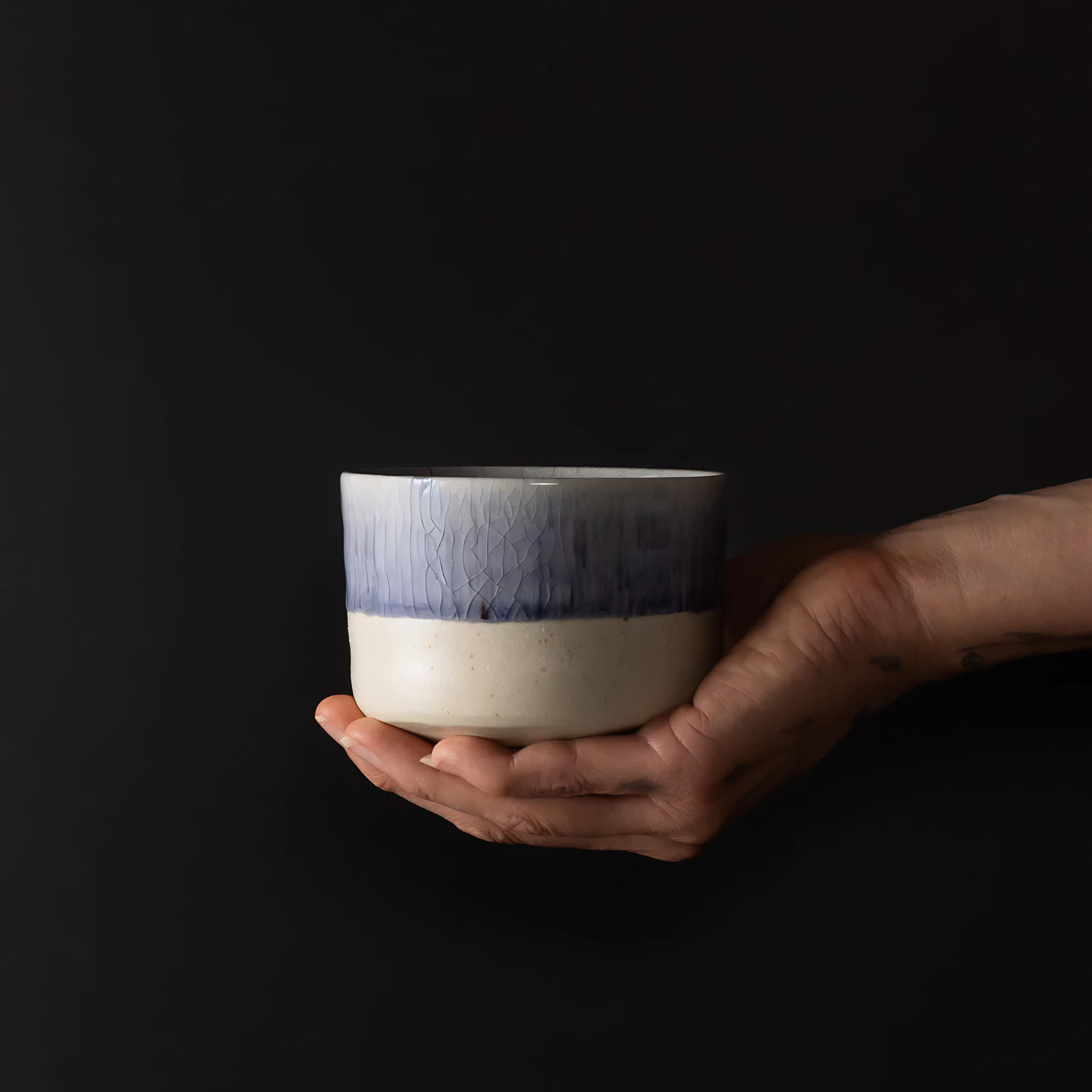 On top of a hand the side view of the Fathom Matcha Tea Bowl 10cm Winter Drift featuring a soft indigo glaze and a delicate speckled texture subtle crackle finish.