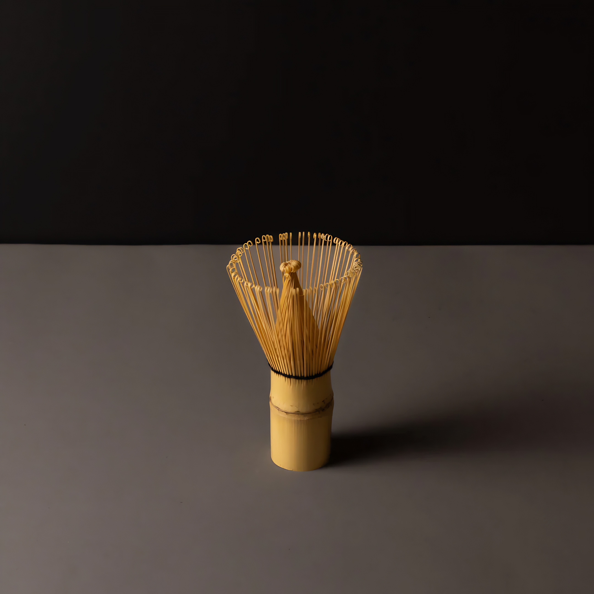 Standing on a surface with a black background the Fathom Matcha Whisk Bamboo 100 Prong, Chasen handcrafted from a single bamboo into delicate bristles making it as whisk