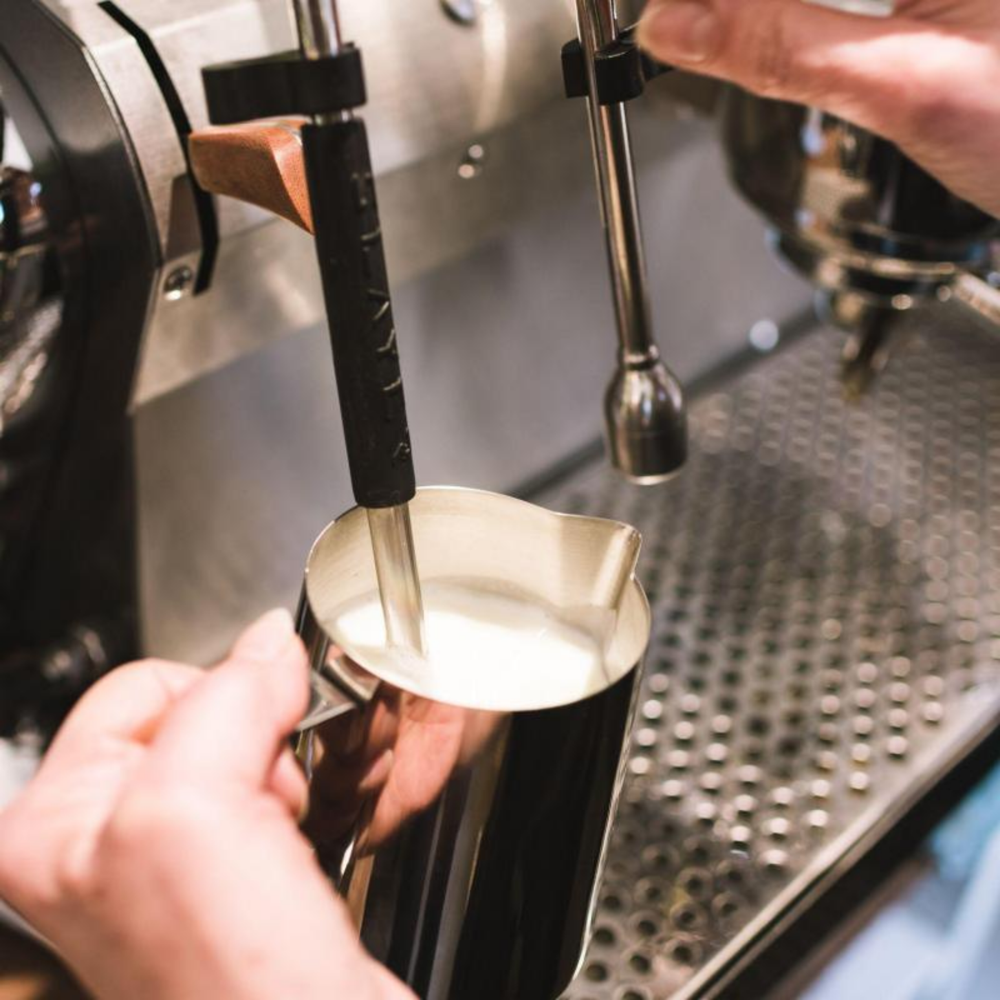 Woman using milk steaming pitcher at coffee machine 