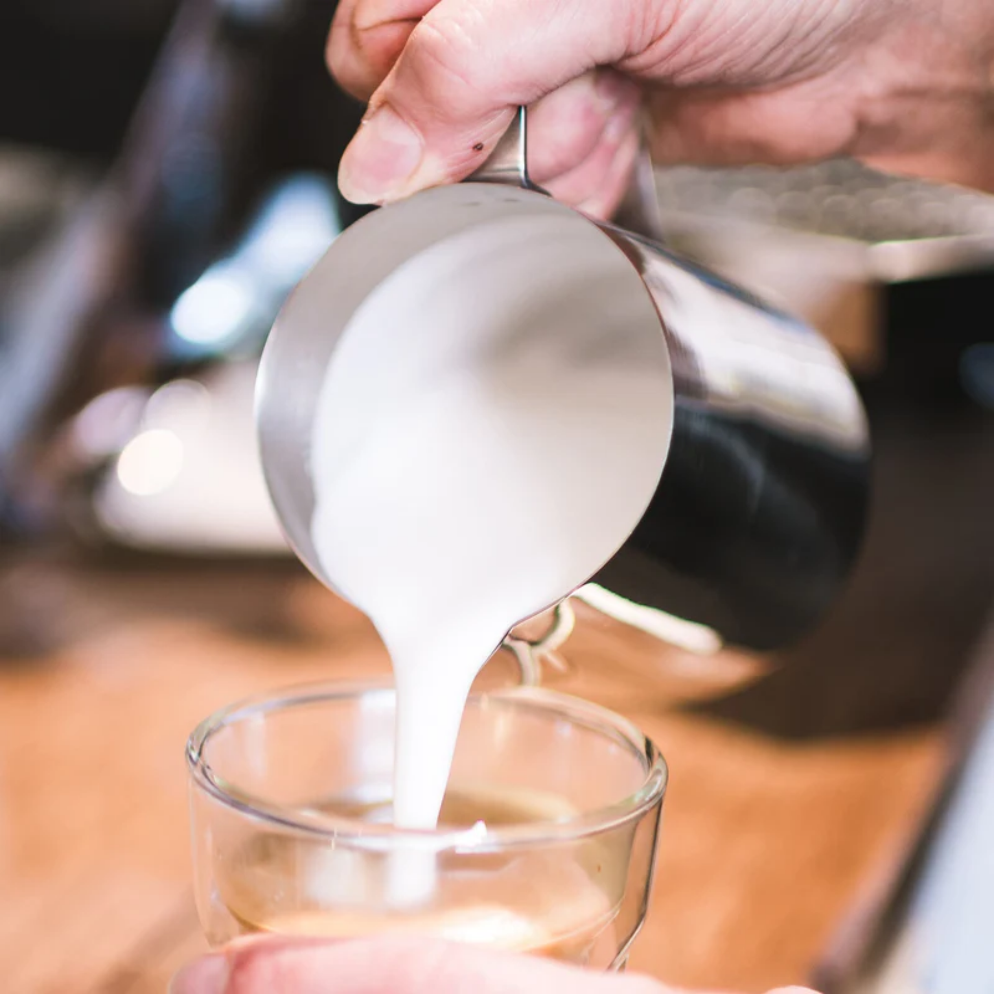 Woman pouring steamed milk into coffee cup