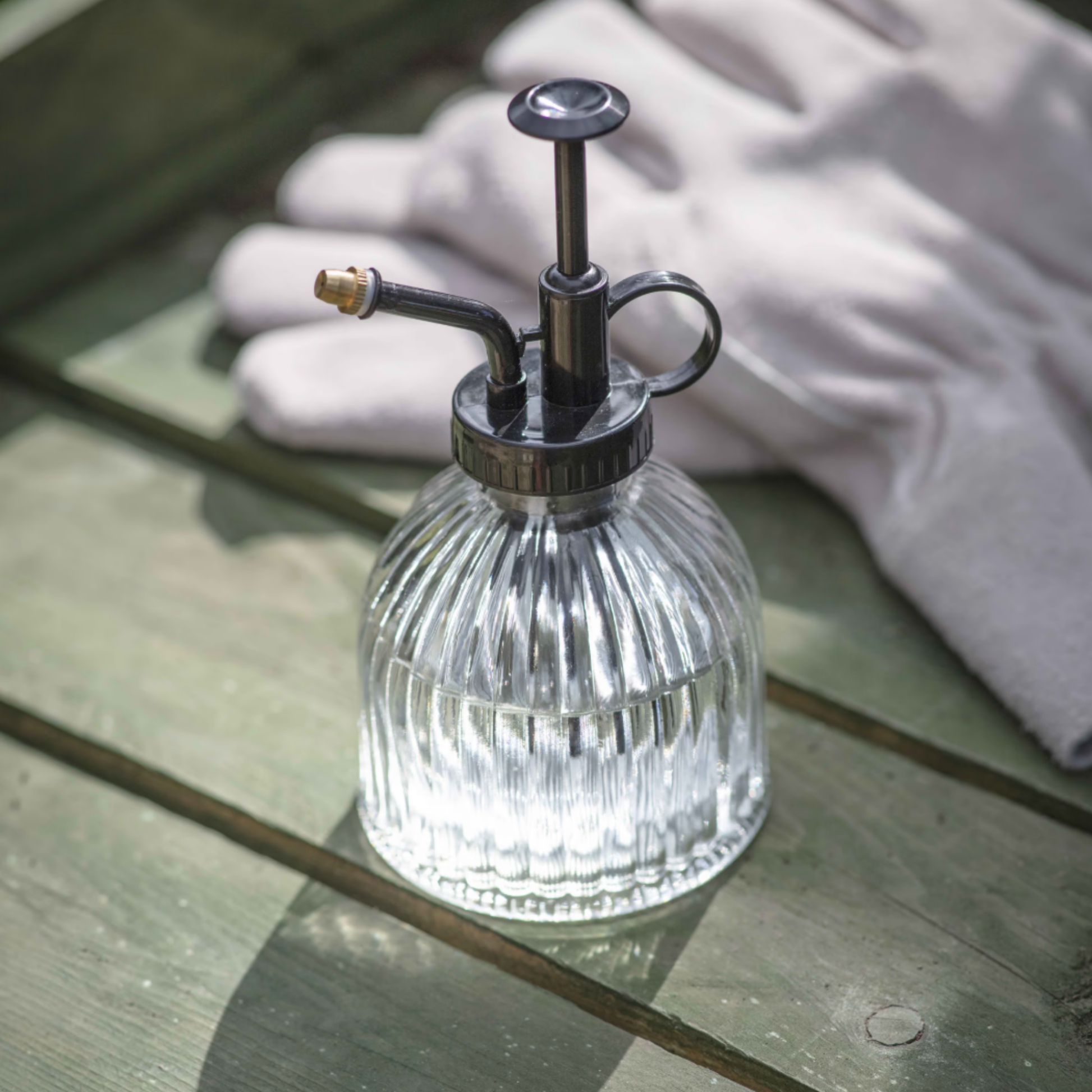 Glass plant mister side angled with black lid and handle on display outside on wooden countertop