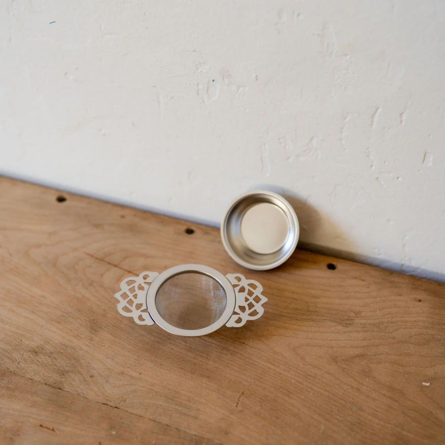 Tea strainer and drip tray side by side top view on wooden table counter top