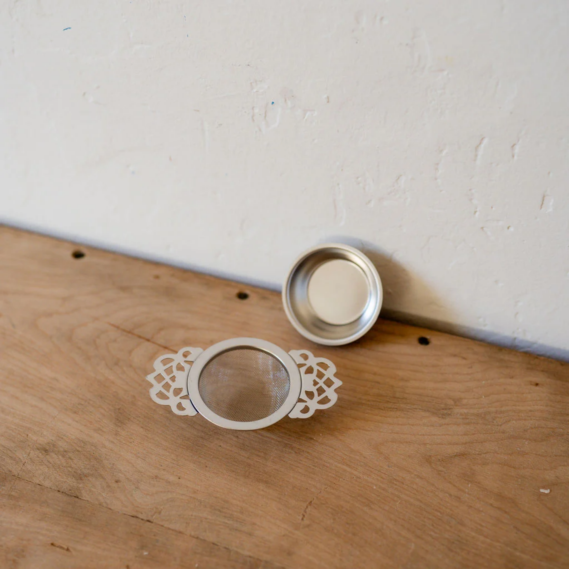 Tea strainer and drip tray side by side top view on wooden table counter top