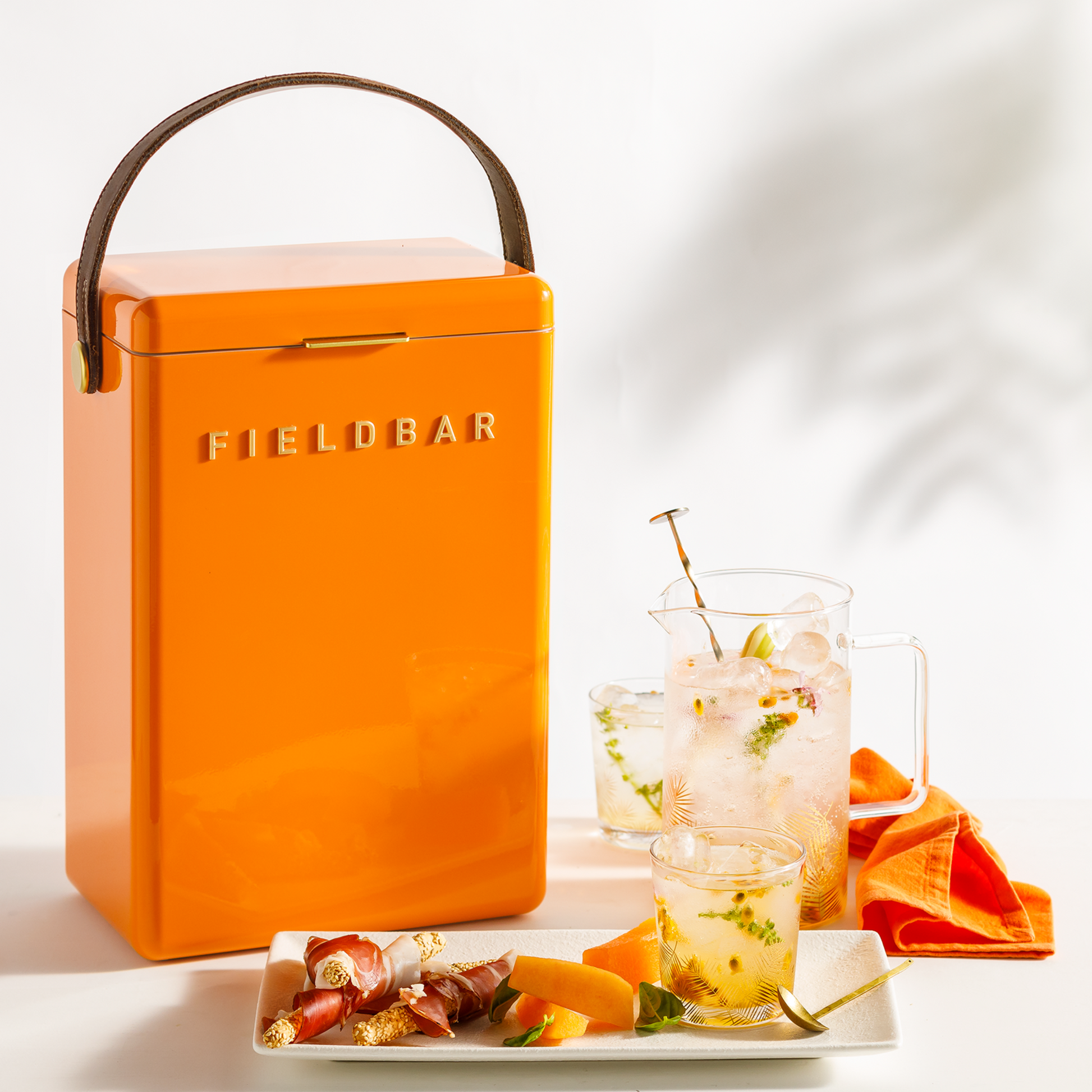 Front view of FIELDBAR Drinks Box MK II hardcase cooler, orchard orange, 10L capacity, durable and comfortable to carry, shown with glasses at the side.