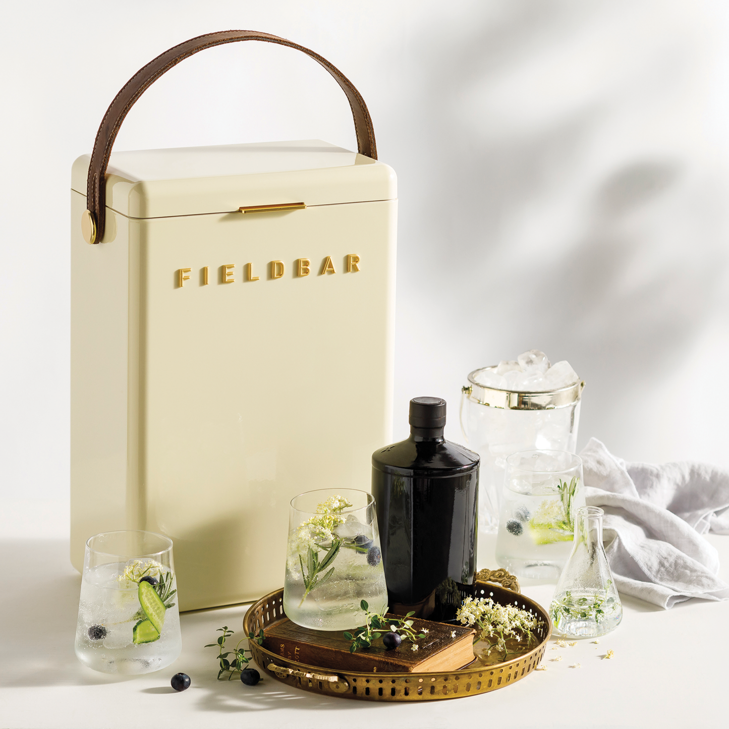 Front view of FIELDBAR Drinks Box MK II hardcase cooler, Safari white, 10L capacity, durable and comfortable to carry, shown with glasses beside it.