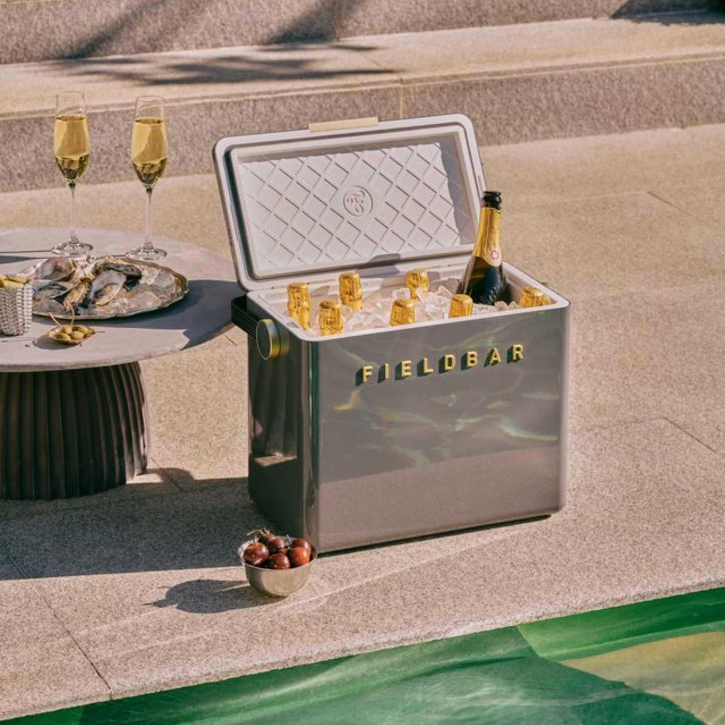 Showing 8 bottles of wine with ice cubes inside the open Fieldbar Gin Trunk hardcase cooler - oyster grey insulated box made with impact-resistant plastic, aluminium hardware, leather-wrapped handle, and BPA-free interior; 24L capacity with 50-hour champagne-cold performance.