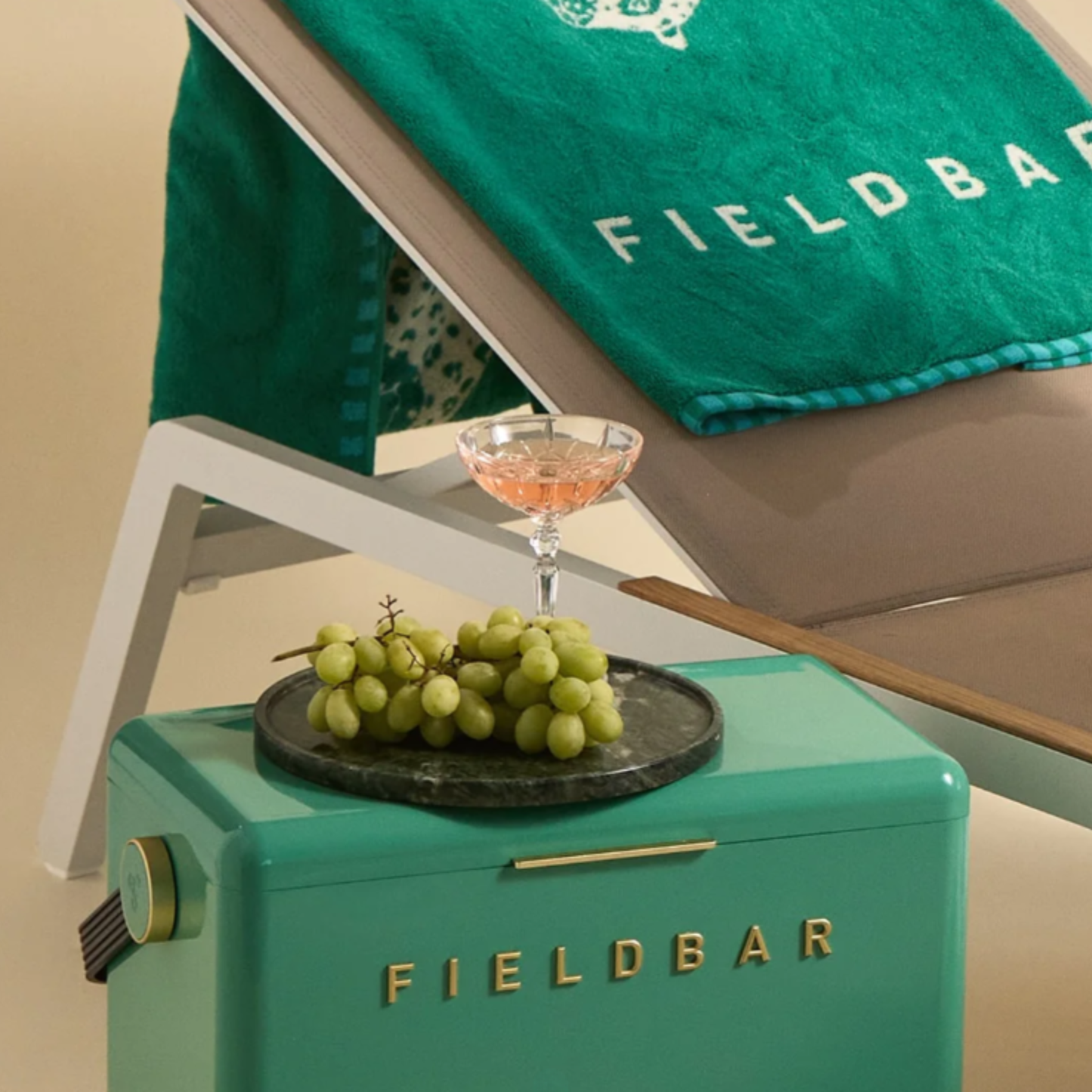 Showing with grapes and drink on top of FIELDBAR Gin Trunk Parisian Green - premium hardcase cooler box in impact-resistant material with genuine leather handle wrap, extruded aluminum handle, reflective paint, airtight gasket, BPA-free interior, and 24L capacity for keeping drinks cold up to 50 hours.