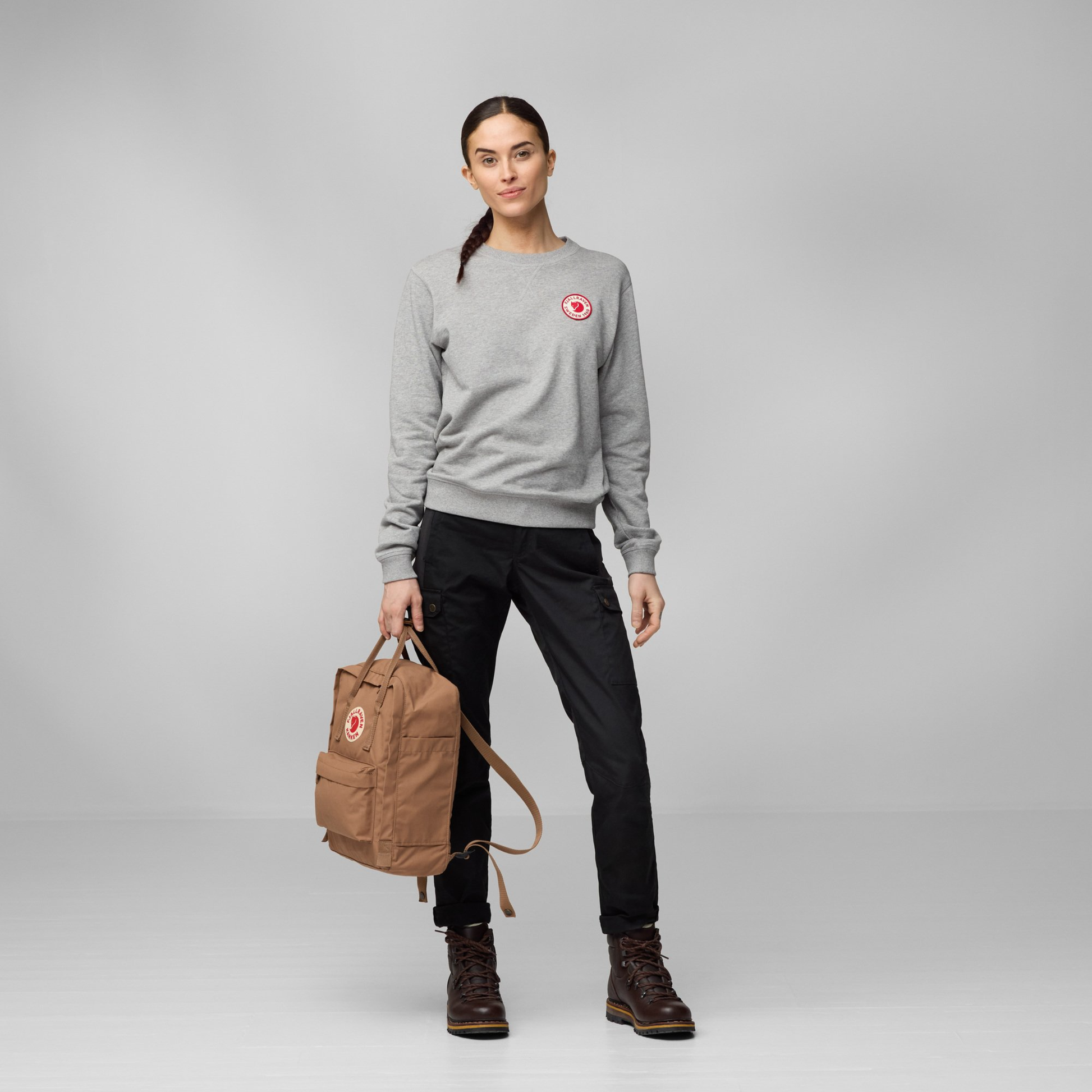 A woman that carried from the top handle The Fjallraven Kanken Backpack which is made from hard-wearing Vinylon F fabric and features a spacious main compartment with a full-length zip, removable PE foam seat cushion, two flat side pockets, a zipped front pocket, adjustable shoulder straps, and top handles. Durable and practical backpack for everyday use.