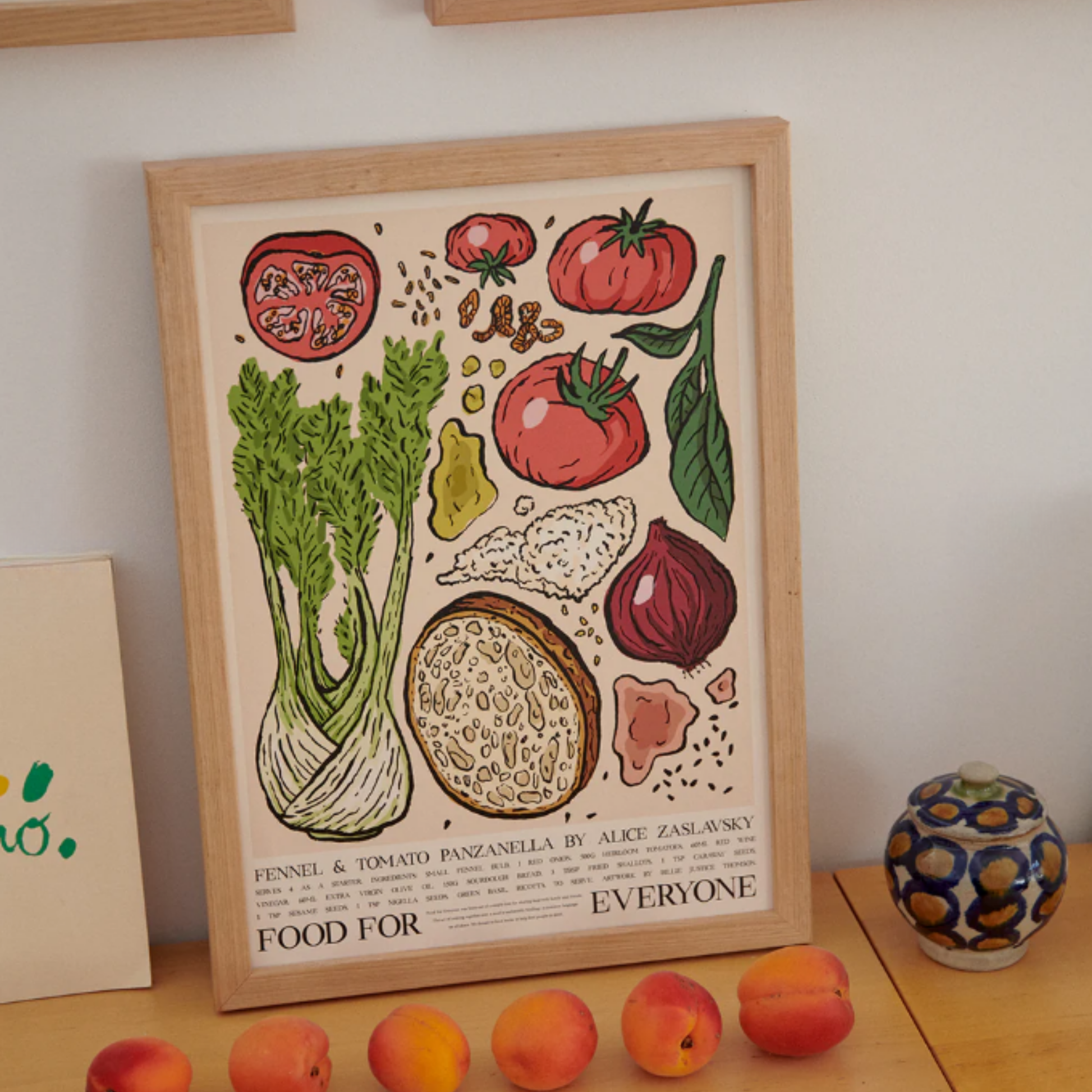 Placed on the surface with fruits for size comparison Food for Everyone Limited Edition Fennel and Tomato Panzanella Poster A2 printed on recycled coffee cup paper, featuring Billie Justice Thomson's colorful artwork inspired by Alice Zaslavsky's vibrant cooking; unframed