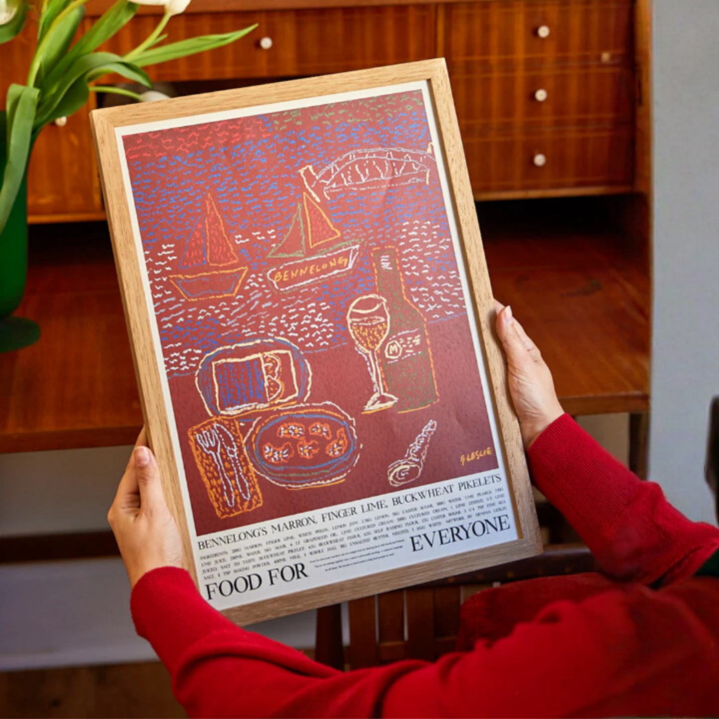 Being held in frame Food for Everyone Bennelong Poster by Gemma Leslie, featuring maroon interiors and Sydney Harbour views inspired by Peter Gilmore's dish; printed on recycled paper, unframed